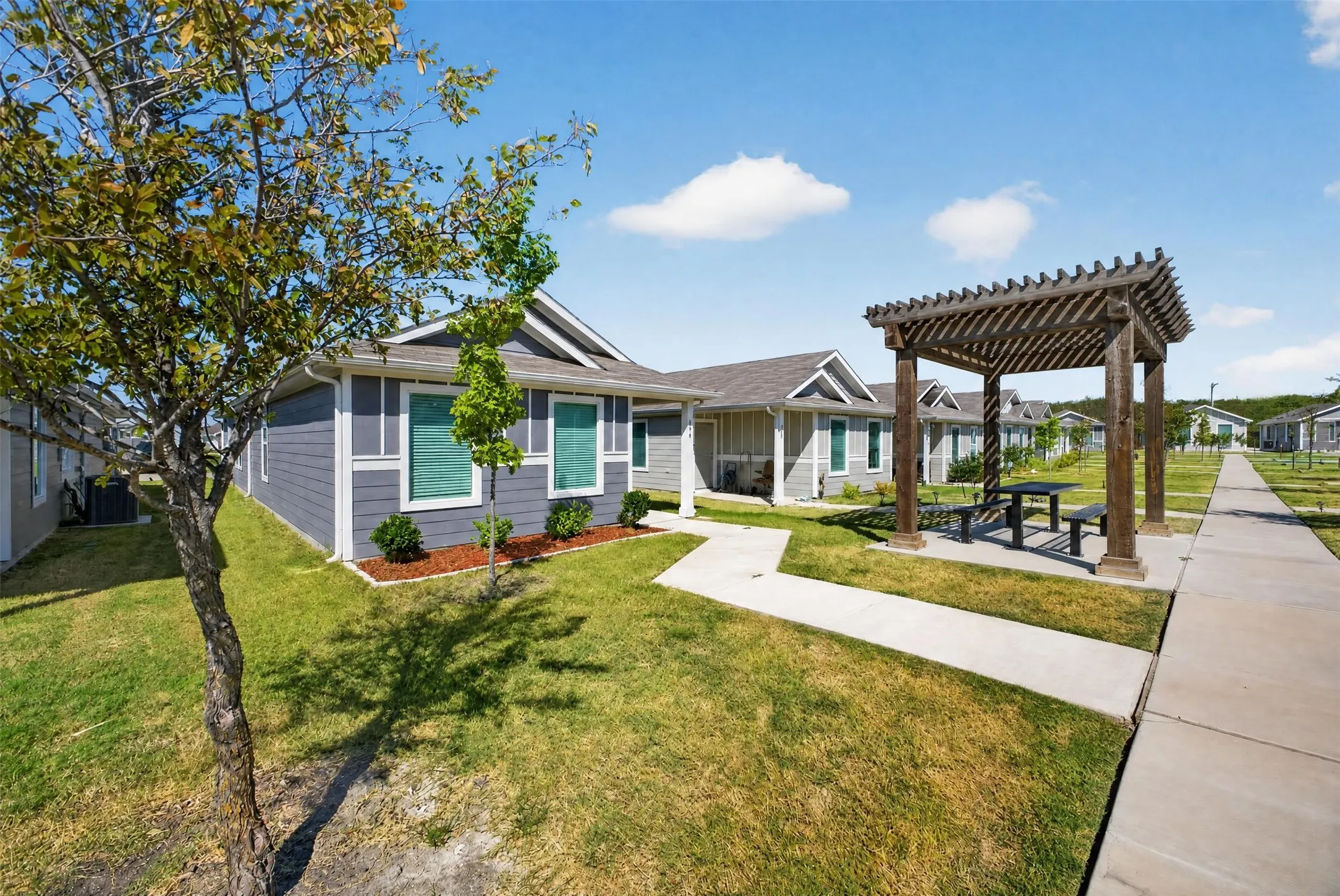 Siding exterior with pitched roof, manicured lawn, and a wood pergola with integrated picnic table