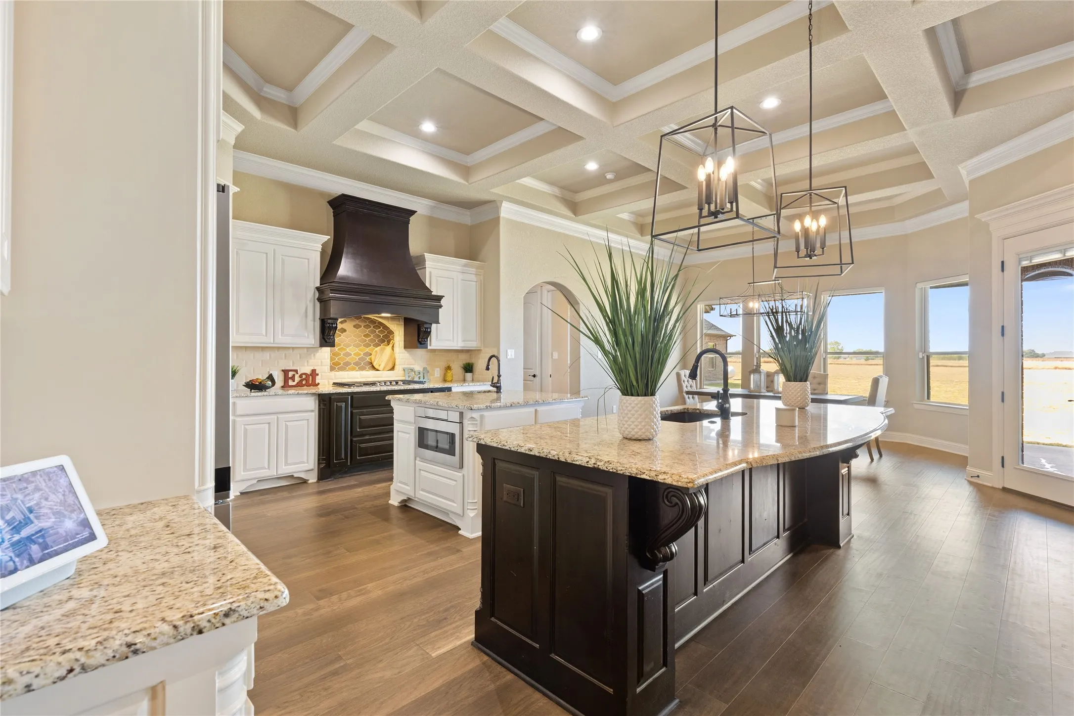 Gourmet kitchen featuring a coffered ceiling, wood-finish flooring, two-tone cabinetry, a large kitchen island with a granite countertop, and pendant lighting