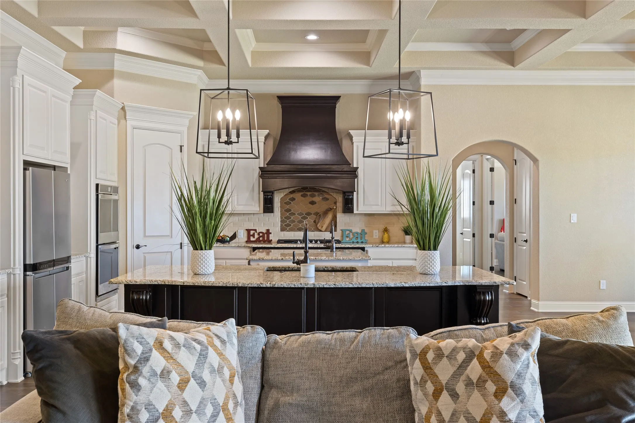 Kitchen featuring a large island with a stone countertop, white upper cabinetry, dark wood lower cabinetry, and stainless steel built-in appliances