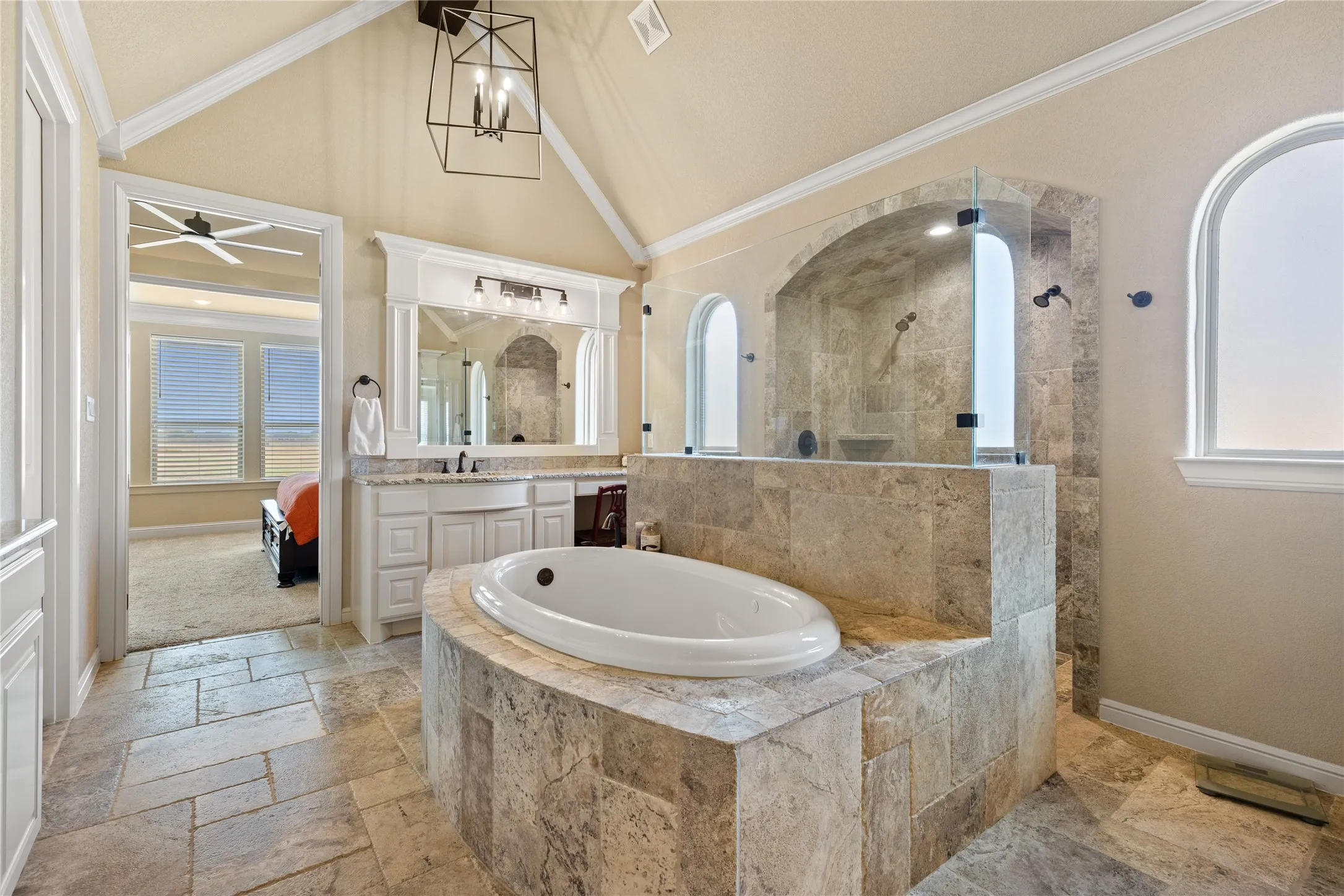 Vaulted ceiling with an architectural light fixture, dual vanity, built-in bathtub with stone surround, and a walk-in shower with arched alcoves
