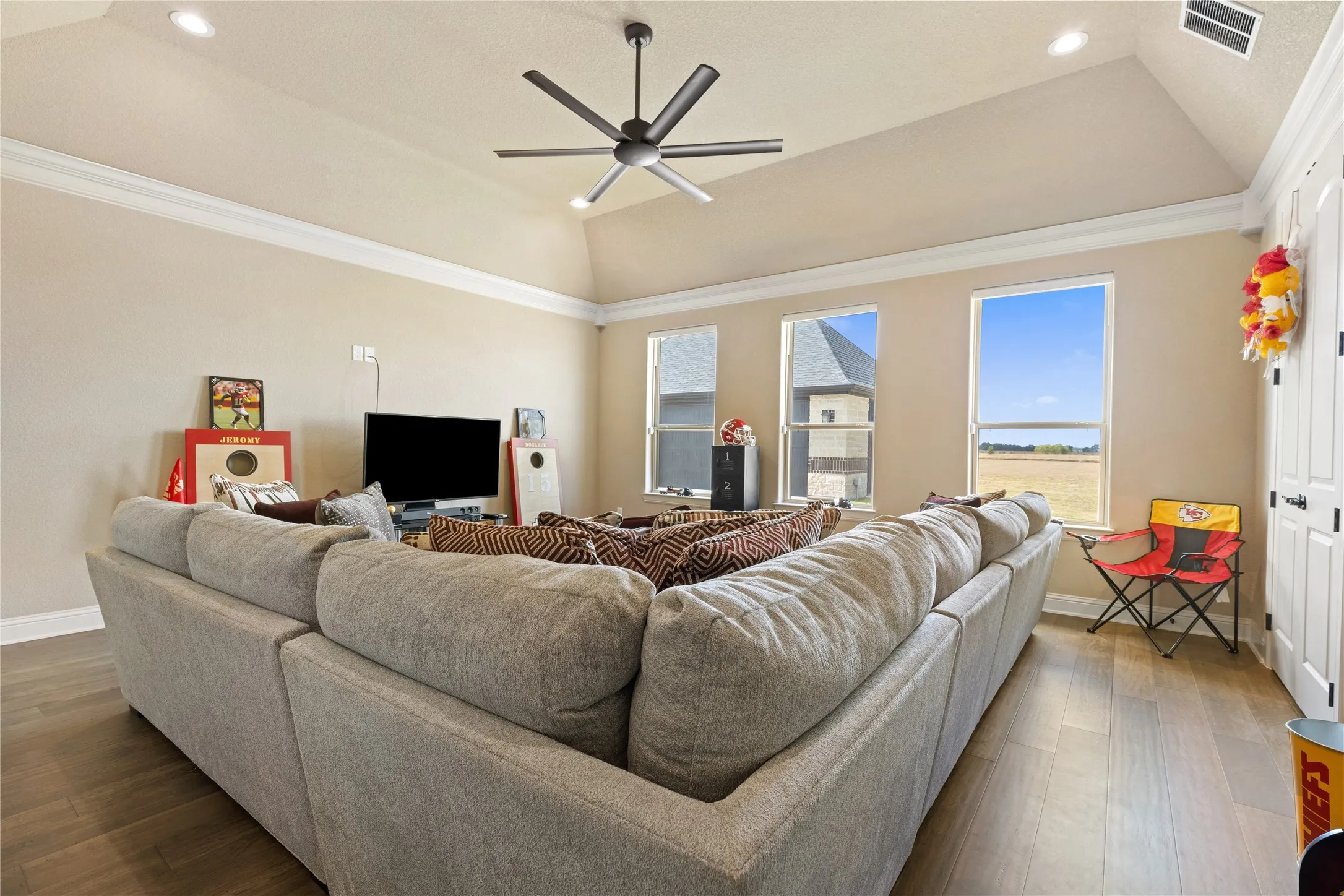 Vaulted ceiling with recessed lighting and a ceiling fan, crown molding, wood-finish flooring, and multiple windows