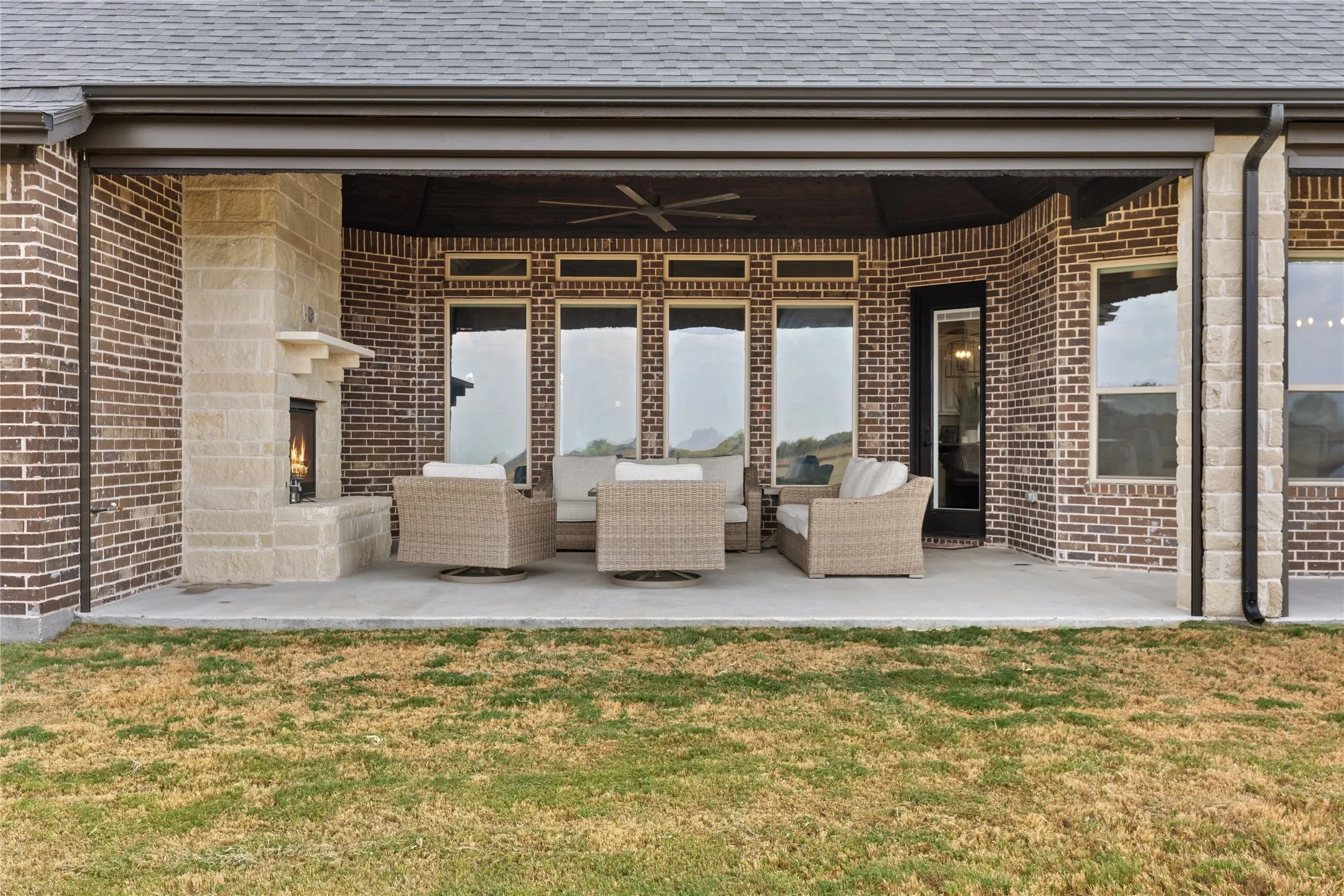Covered patio featuring a stone-clad fireplace, brick exterior, and multiple large windows with motorized screens