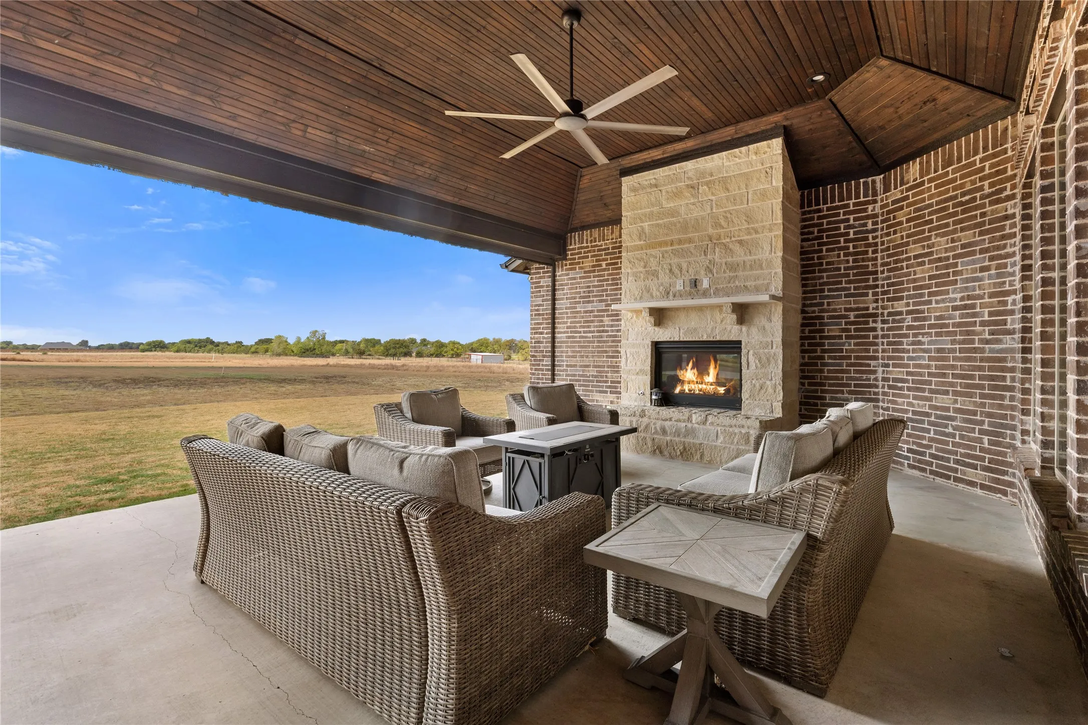 Covered patio featuring a wood-panel ceiling, brick and stone fireplace, ceiling fan, and concrete flooring