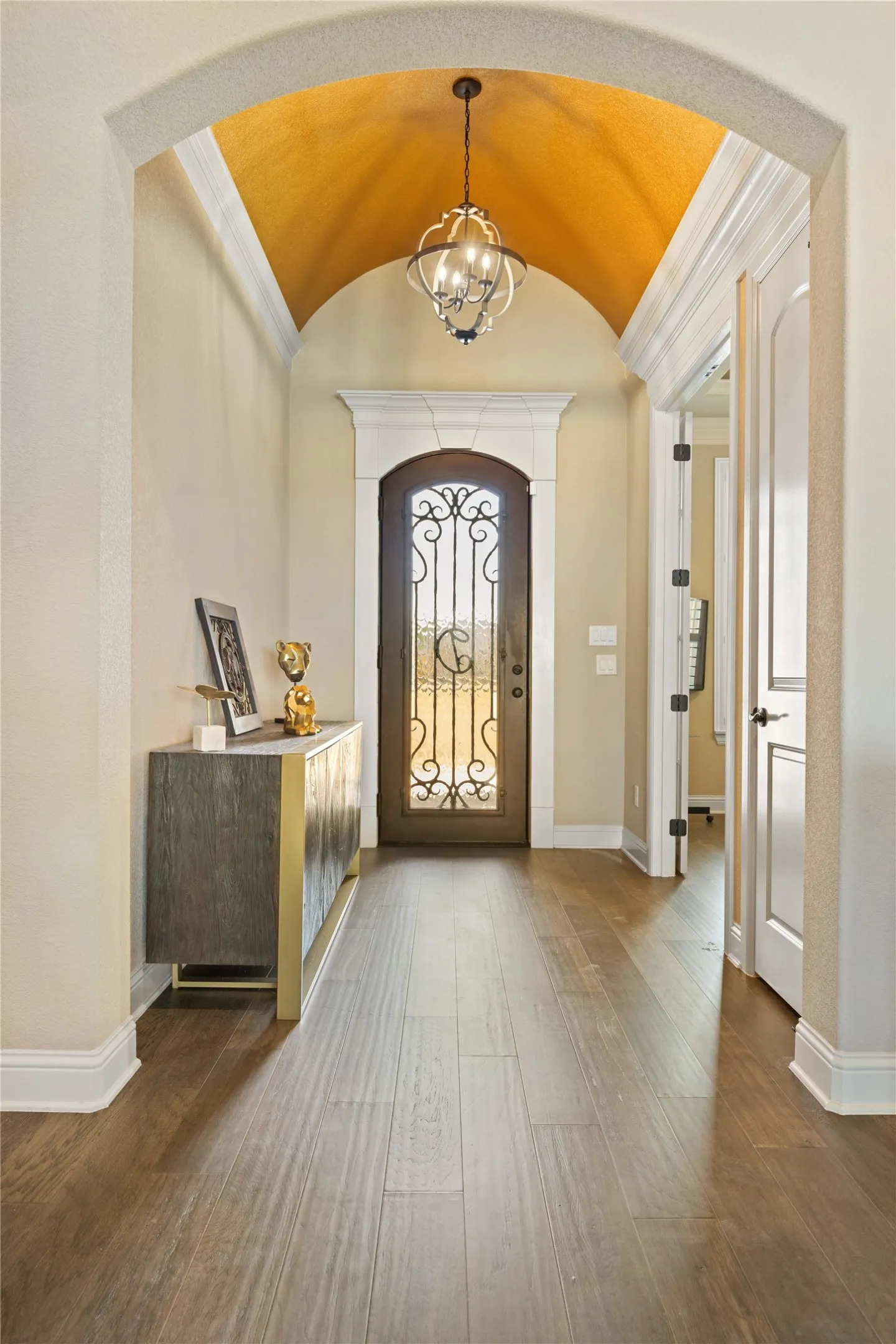Arched entryway featuring a decorative chandelier, vaulted ceiling, wood-finish flooring, and a glass-paneled entry door with intricate wrought iron detailing