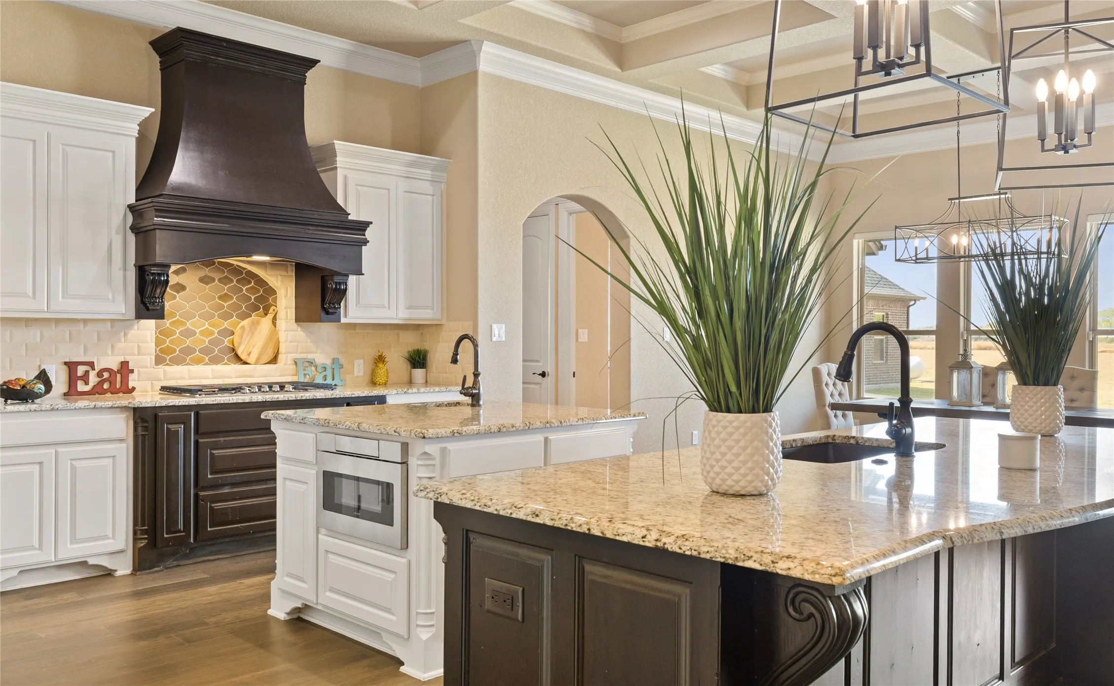 Gourmet kitchen featuring a dark wood range hood, two-tone cabinetry, light-toned countertops, and a coffered ceiling
