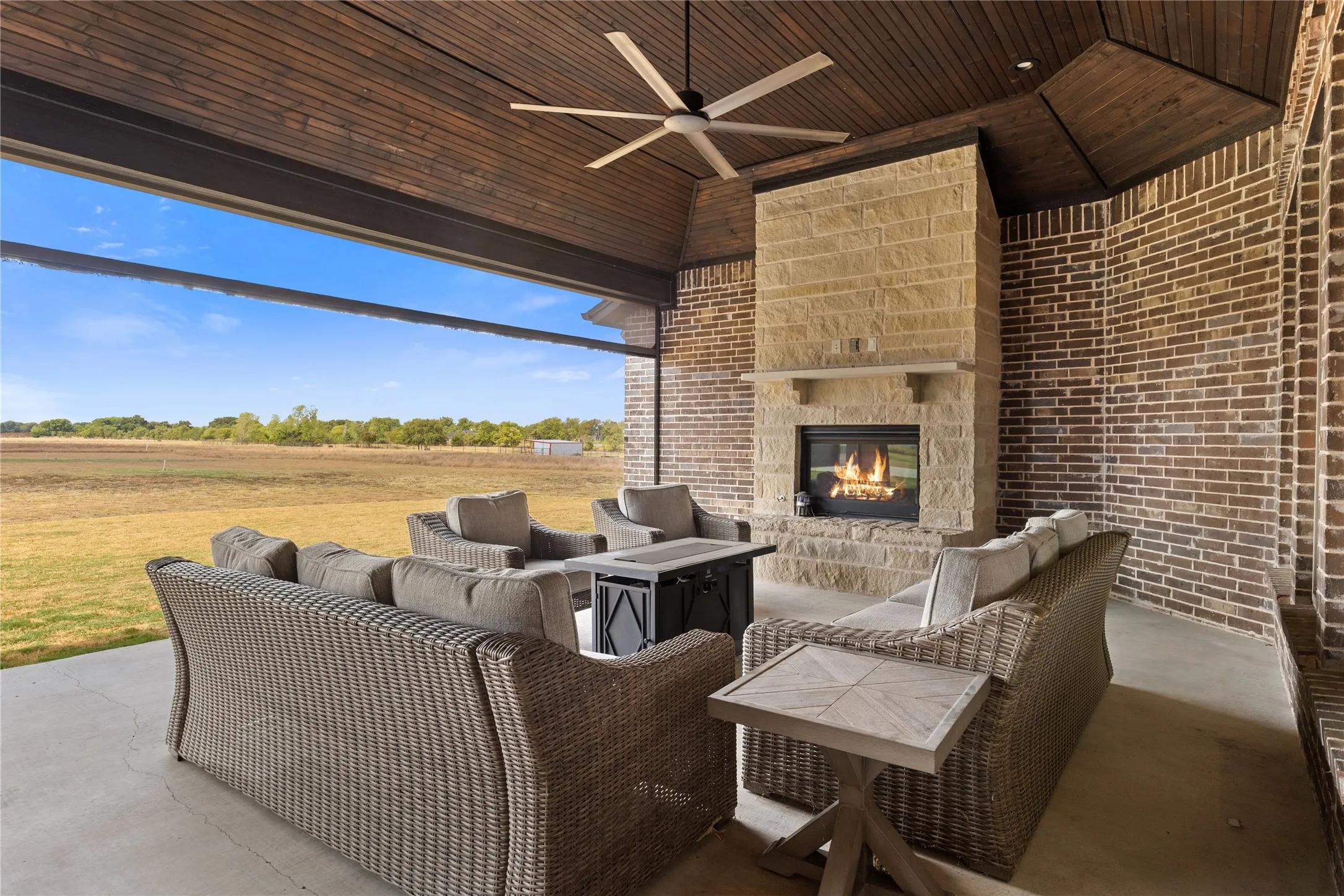 Covered patio featuring a wood-panel ceiling and an outdoor fireplace with a stone surround with motorized screens