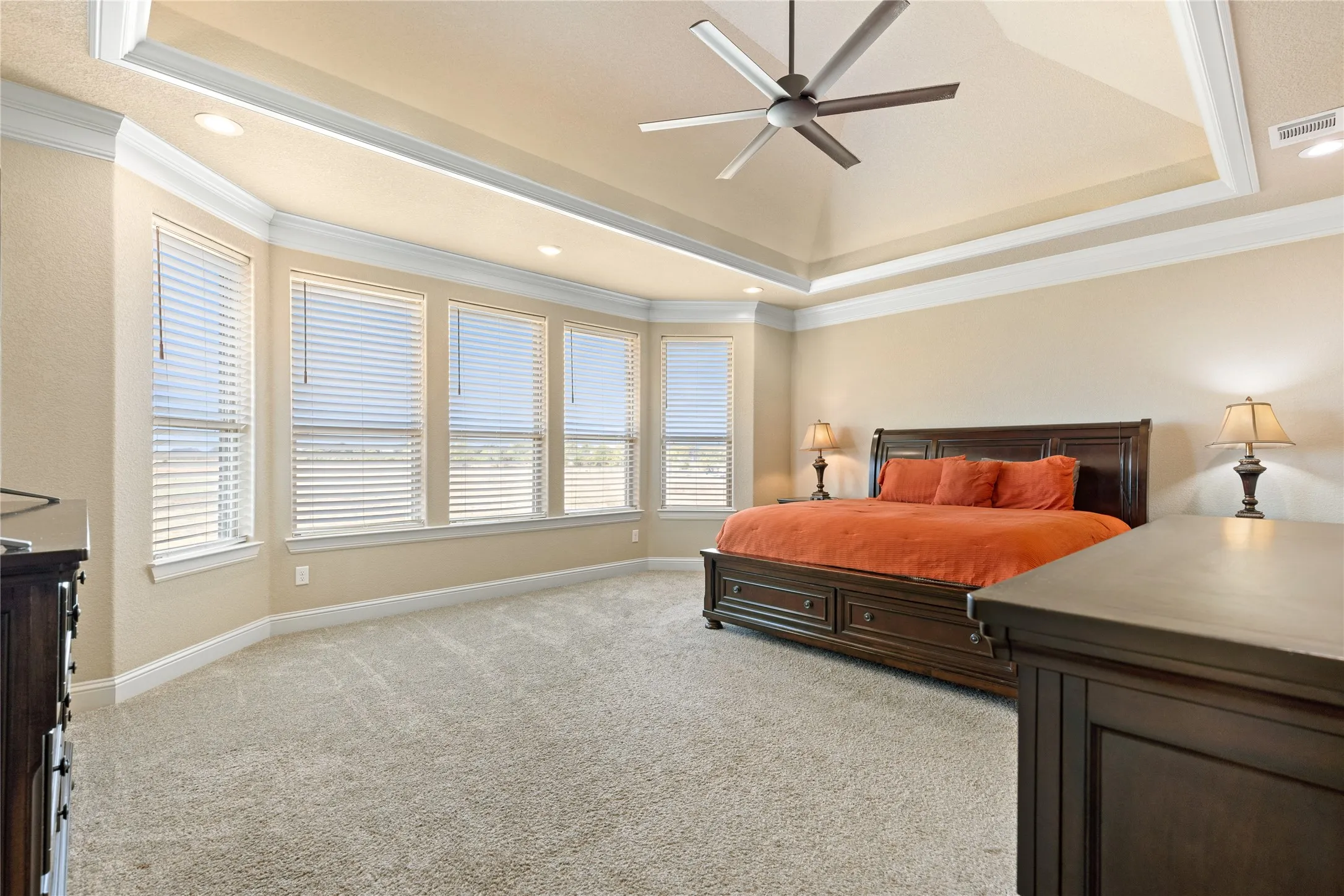 Recessed lighting, ceiling fan, tray ceiling, bay window with multiple windows, and neutral carpet flooring