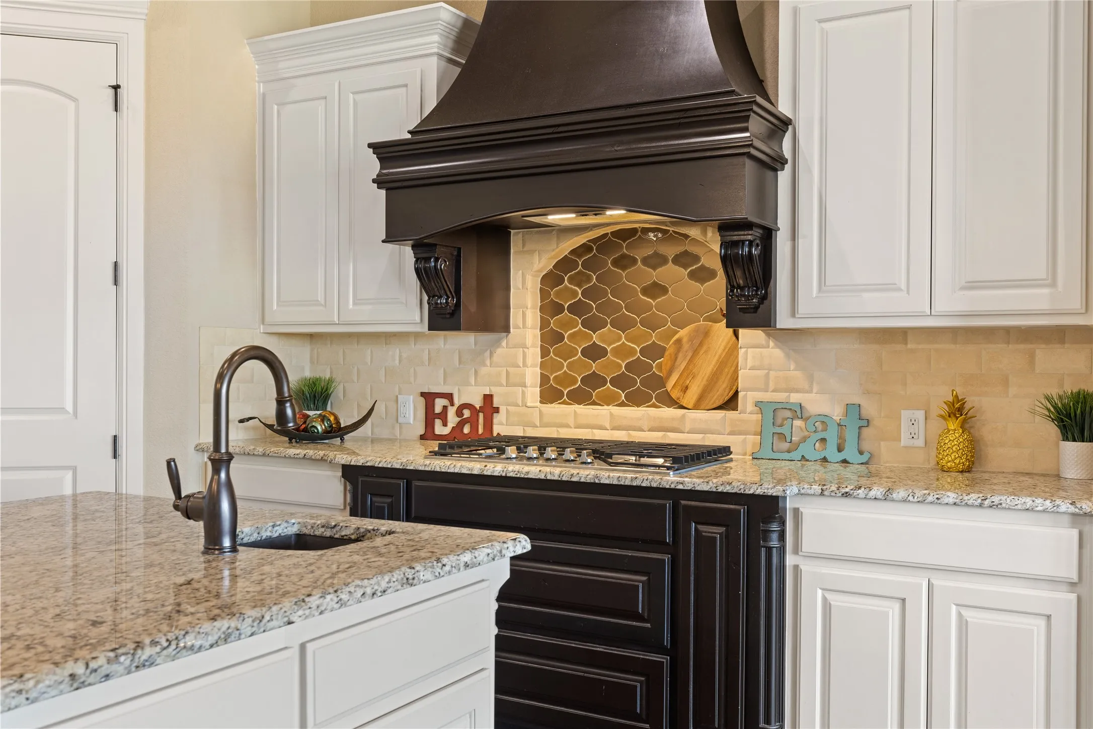Granite countertops, white upper cabinetry, dark wood finish lower cabinetry, subway tile backsplash, and an arched niche with mosaic tile