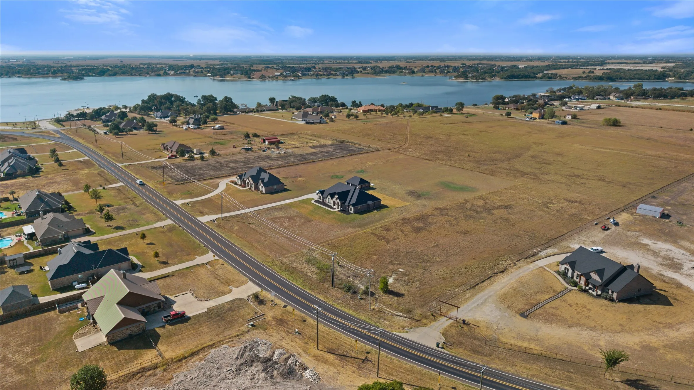 Expansive land parcel featuring a paved road, scattered residences, and a distant body of water