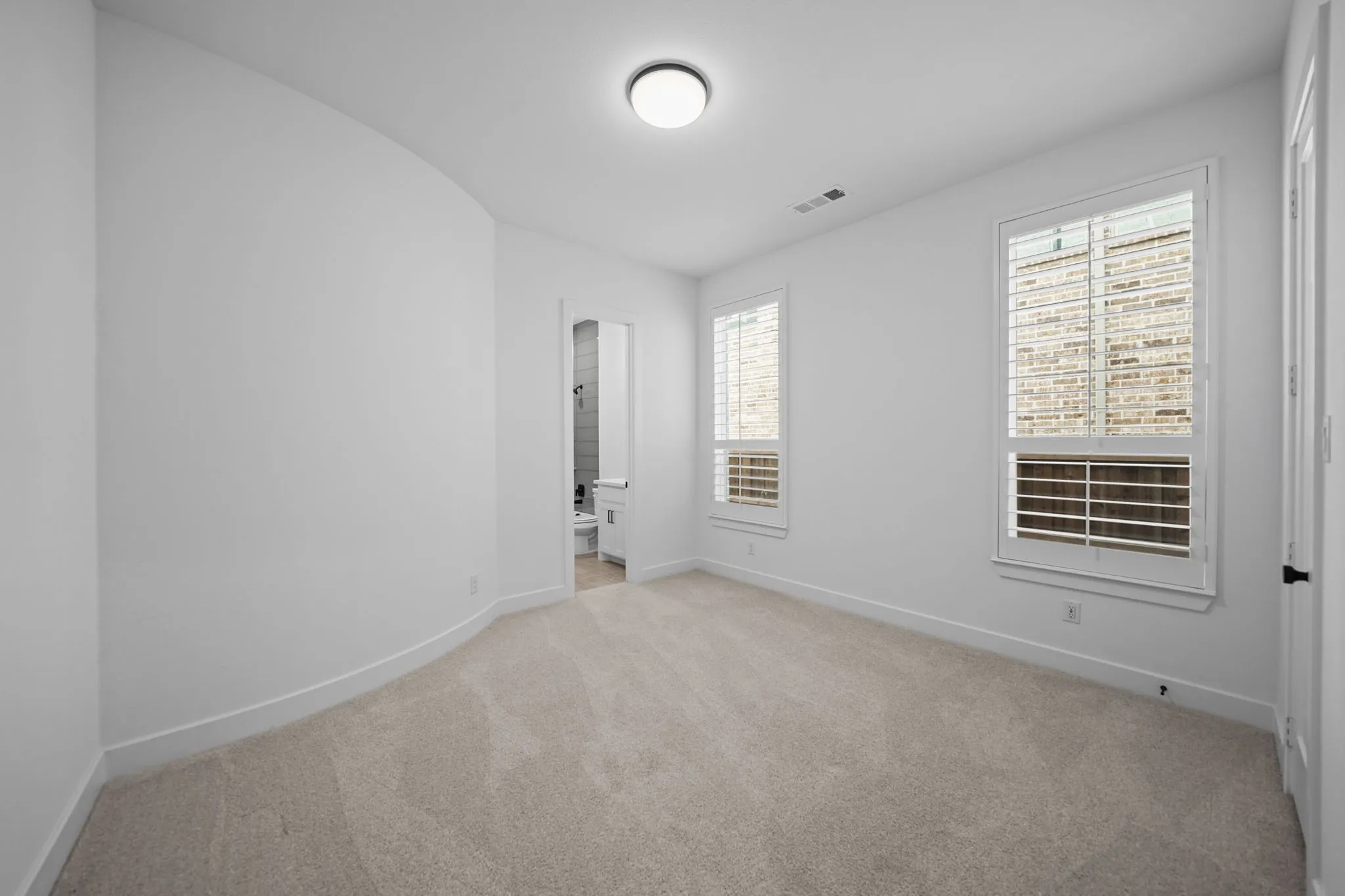 1st floor guestroom with white walls, two windows featuring plantation shutters, and a ceiling-mounted light fixture