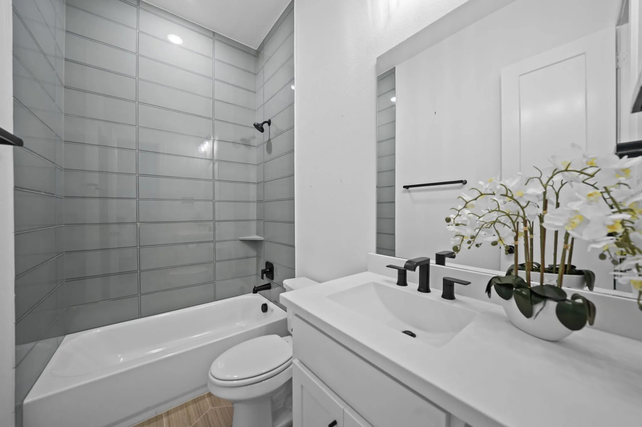 Downstairs guest bedroom en-suite bathroom featuring a white vanity with integrated sink, matte black fixtures, a full-width mirror, and a white bathtub with subway tile surround
