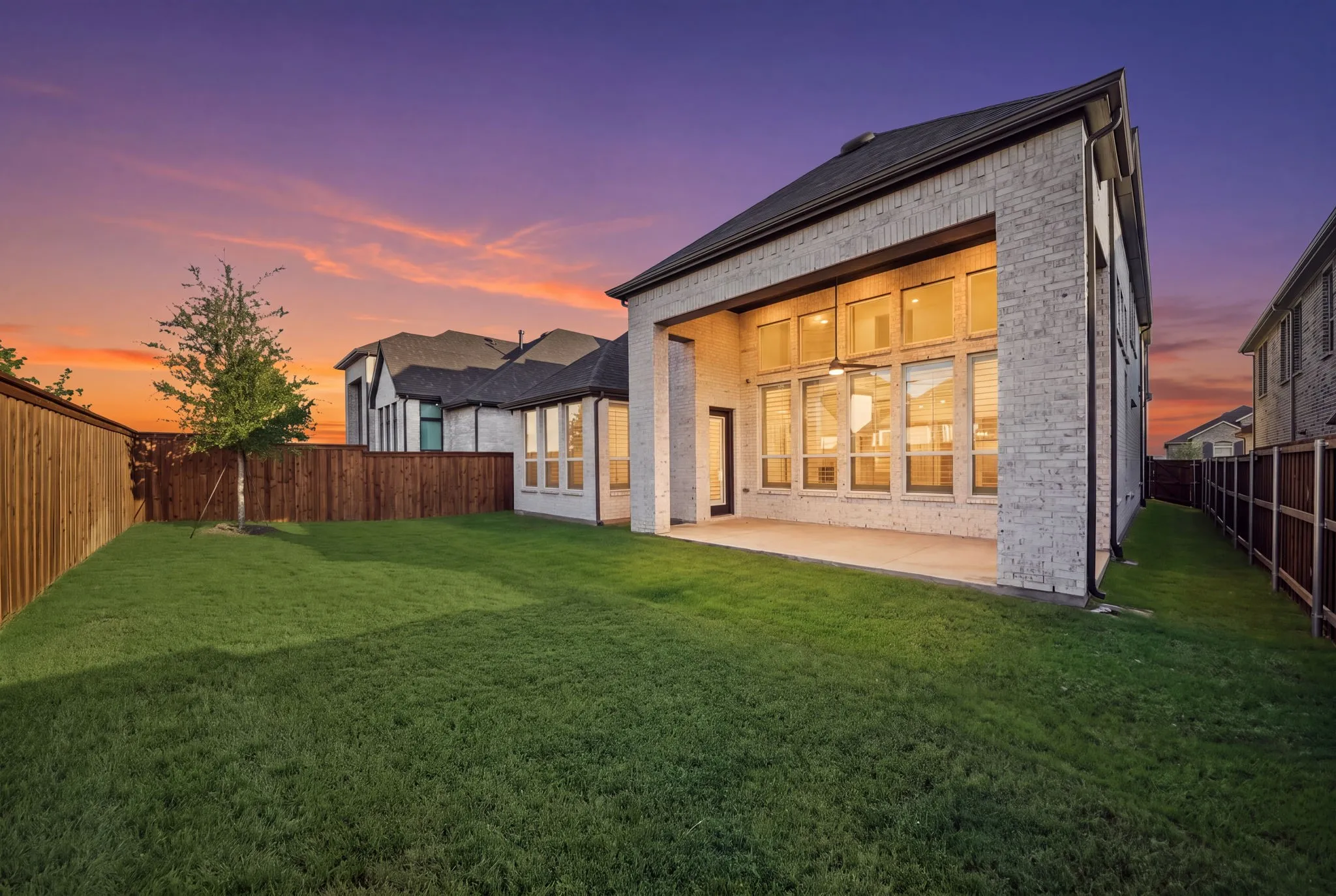 Expansive backyard with a manicured lawn, full privacy fencing, and a covered patio