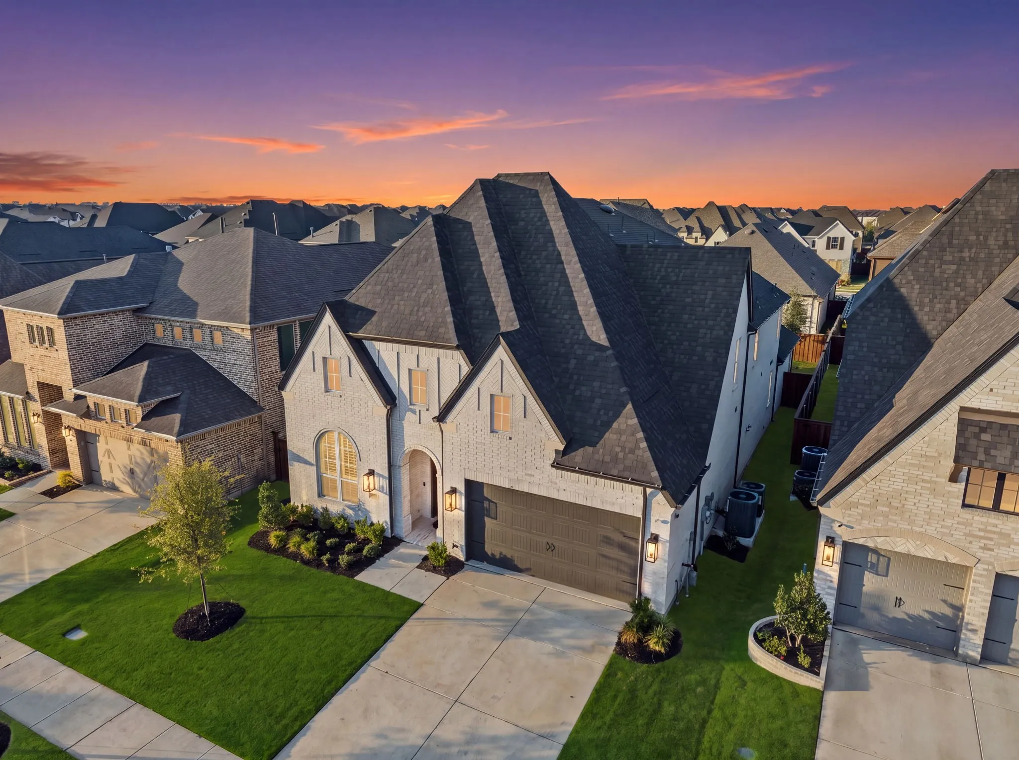 Light-colored brick exterior with dark trim accents, attached two-car garage, manicured front lawn, concrete driveway, and covered front entry