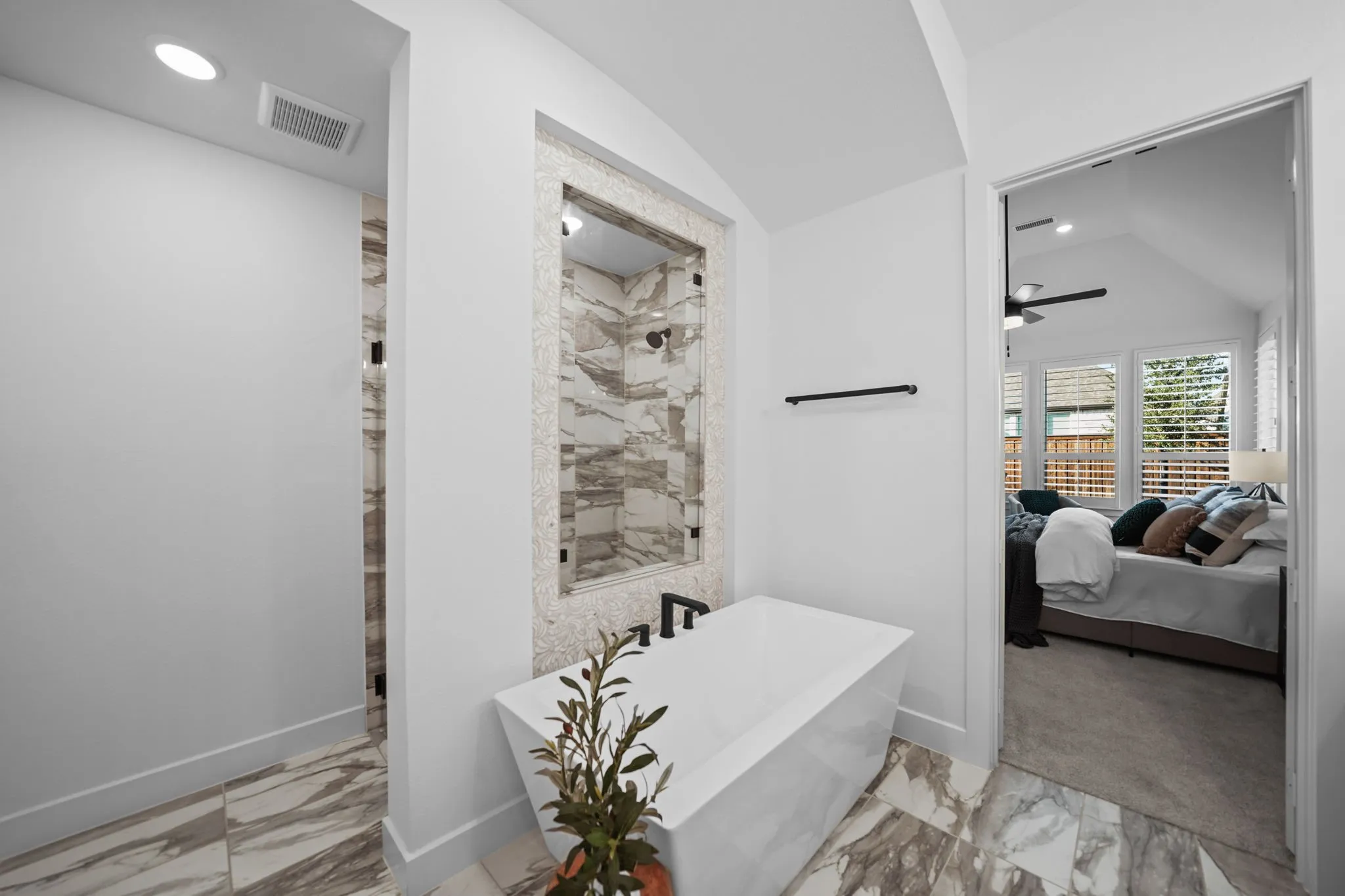 Freestanding soaking tub with matte black fixtures, set against a tiled accent wall shower with glass enclosure