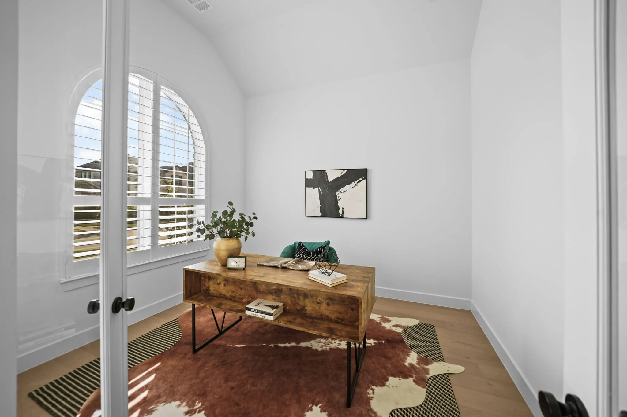 Arched window with plantation shutters, vaulted ceiling, wood-finish flooring, and glass-paneled entry door