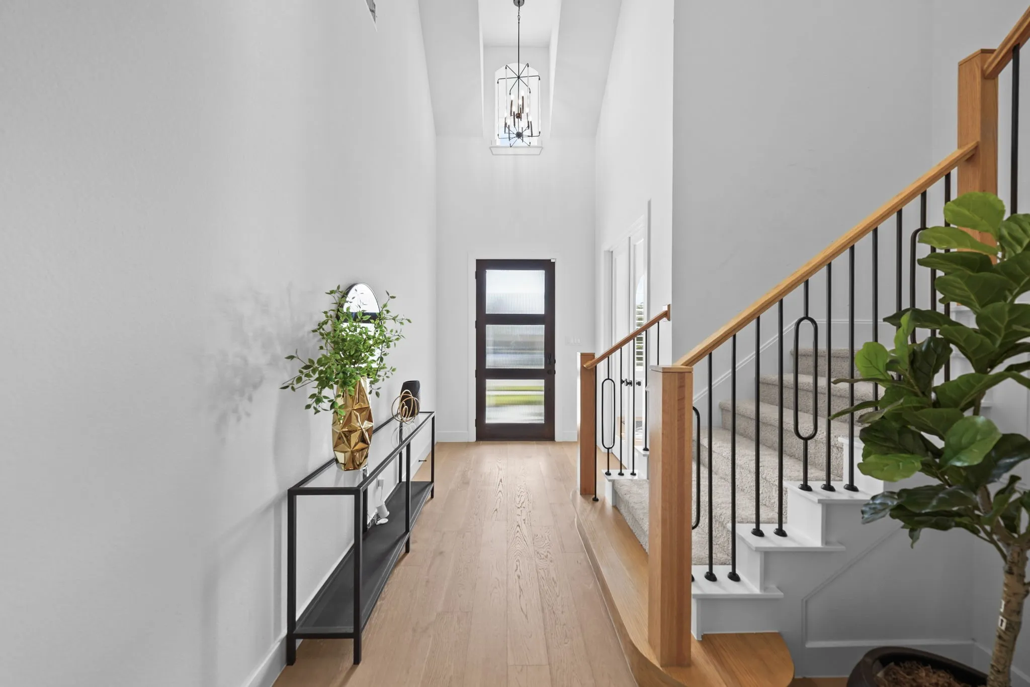 Vaulted entry featuring wood-finish flooring, a contemporary chandelier, and a staircase with wood railings and black metal balusters