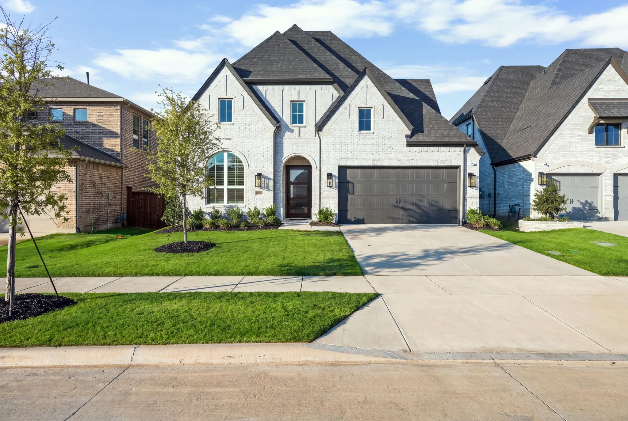 White brick exterior with dark trim, arched entryway, and a two-car garage