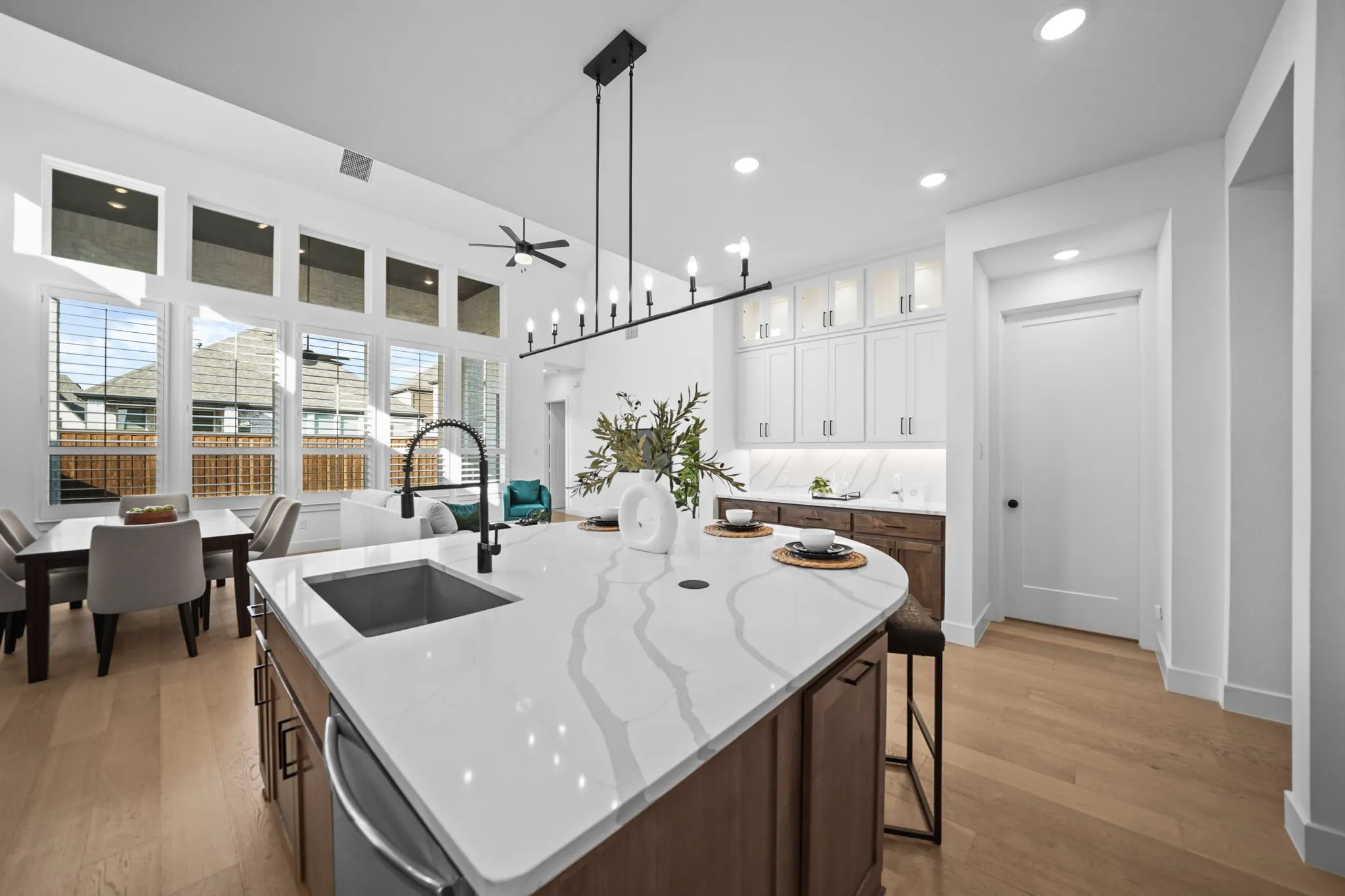 Expansive kitchen island with a waterfall edge and integrated sink, light wood-finish flooring, vaulted ceiling, recessed lighting, and a linear chandelier