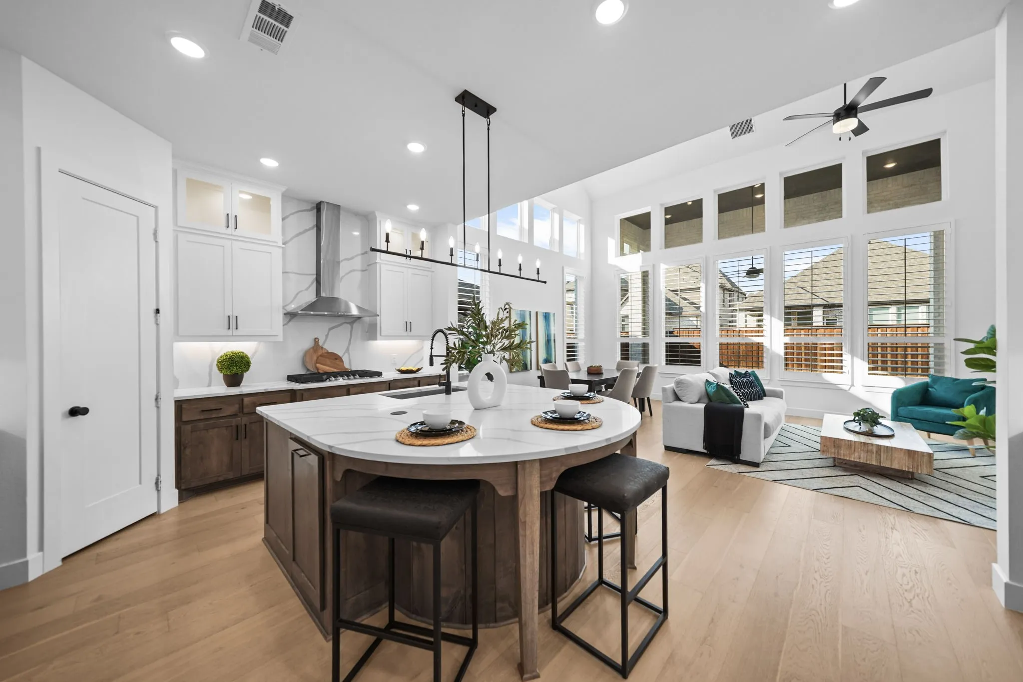 Open-concept living space with wood-finish flooring, two-story windows, and a ceiling fan