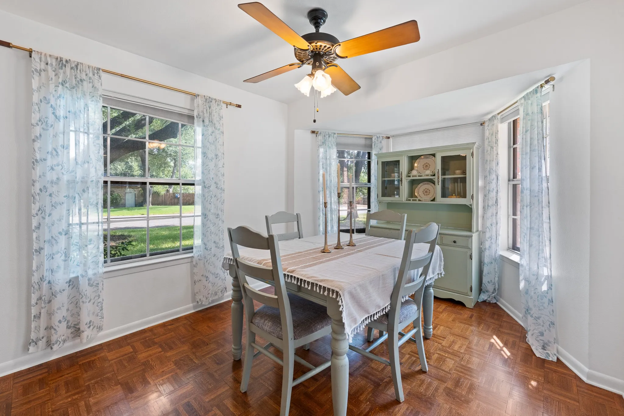 Parquet wood-finish flooring, recessed bay windows, a ceiling fan with integrated lighting, and a built-in display cabinet