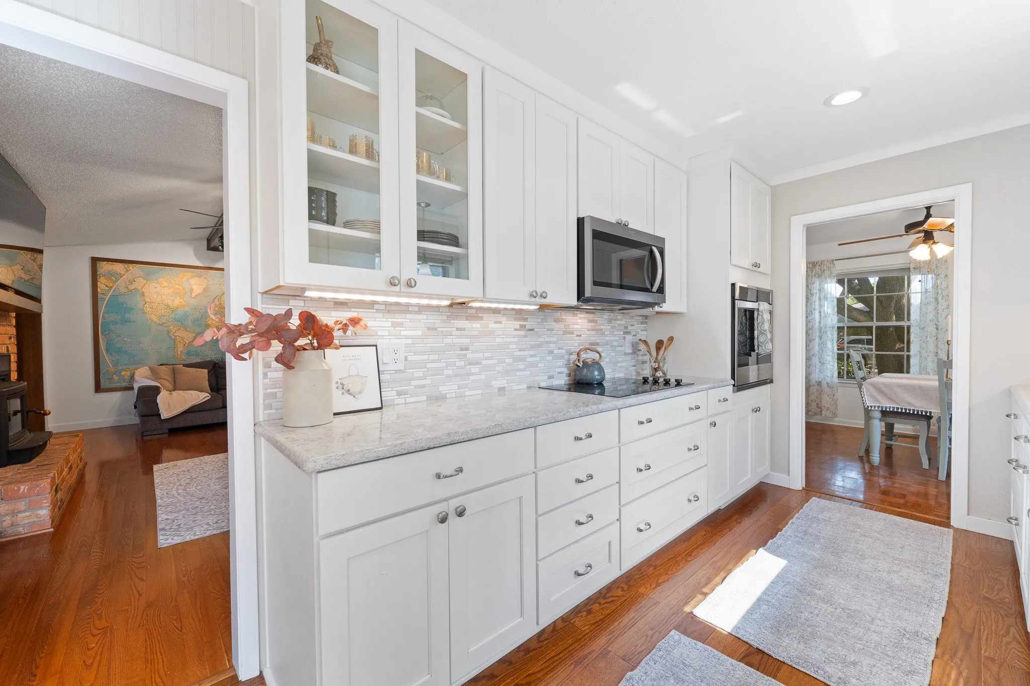 White cabinetry with glass-front upper cabinets, light-toned countertop, and tile backsplash
