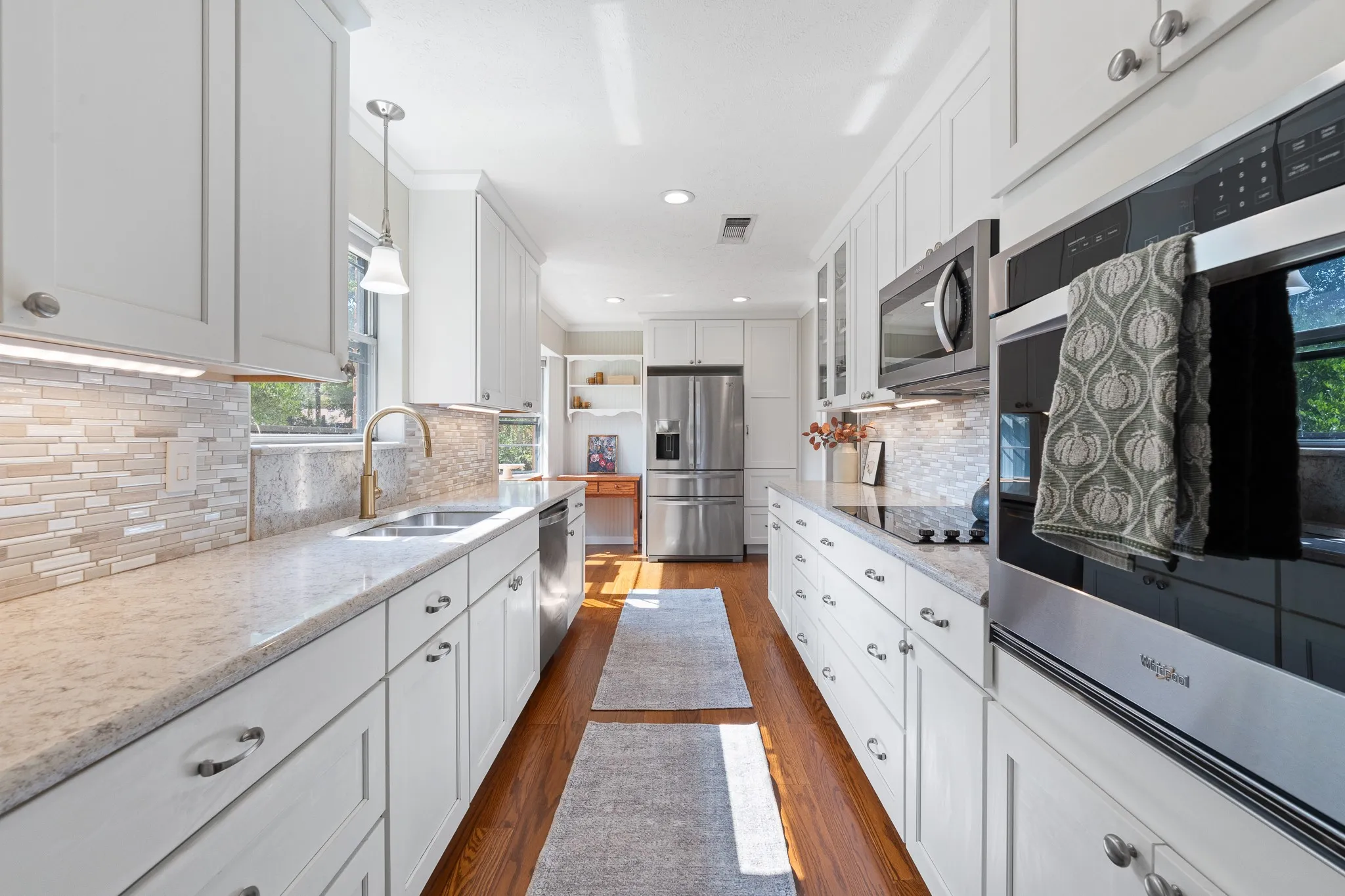 White cabinetry with brushed nickel hardware, stainless steel appliances, wood-finish flooring, undermount sink with a gooseneck faucet, and mosaic tile backsplash