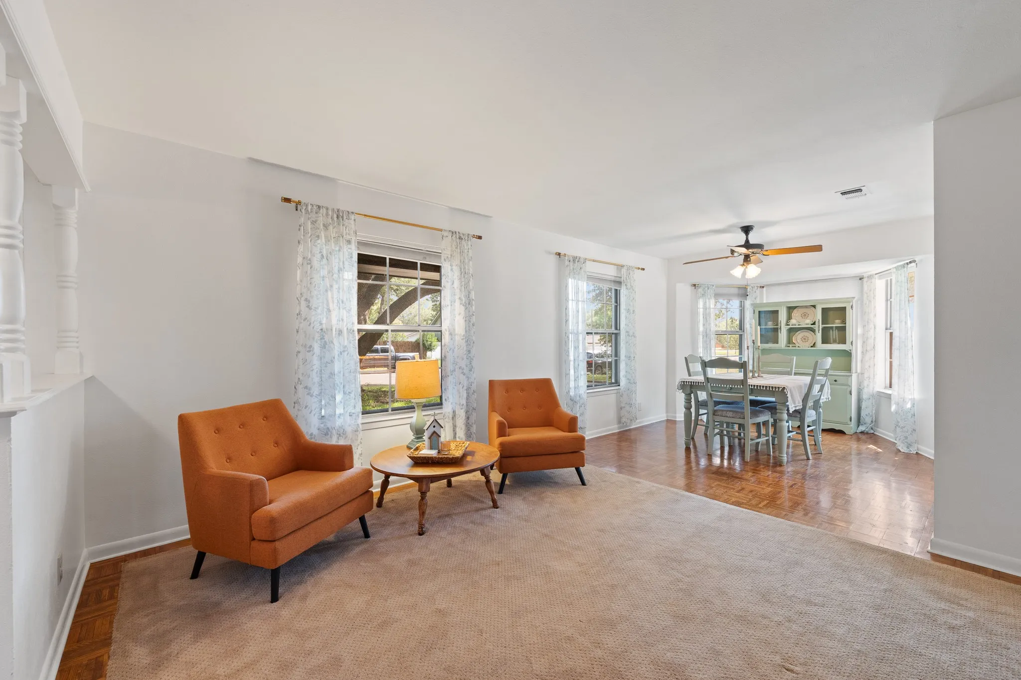 Open-concept living space featuring a carpeted area, wood-finish flooring, multiple windows, and a ceiling fan