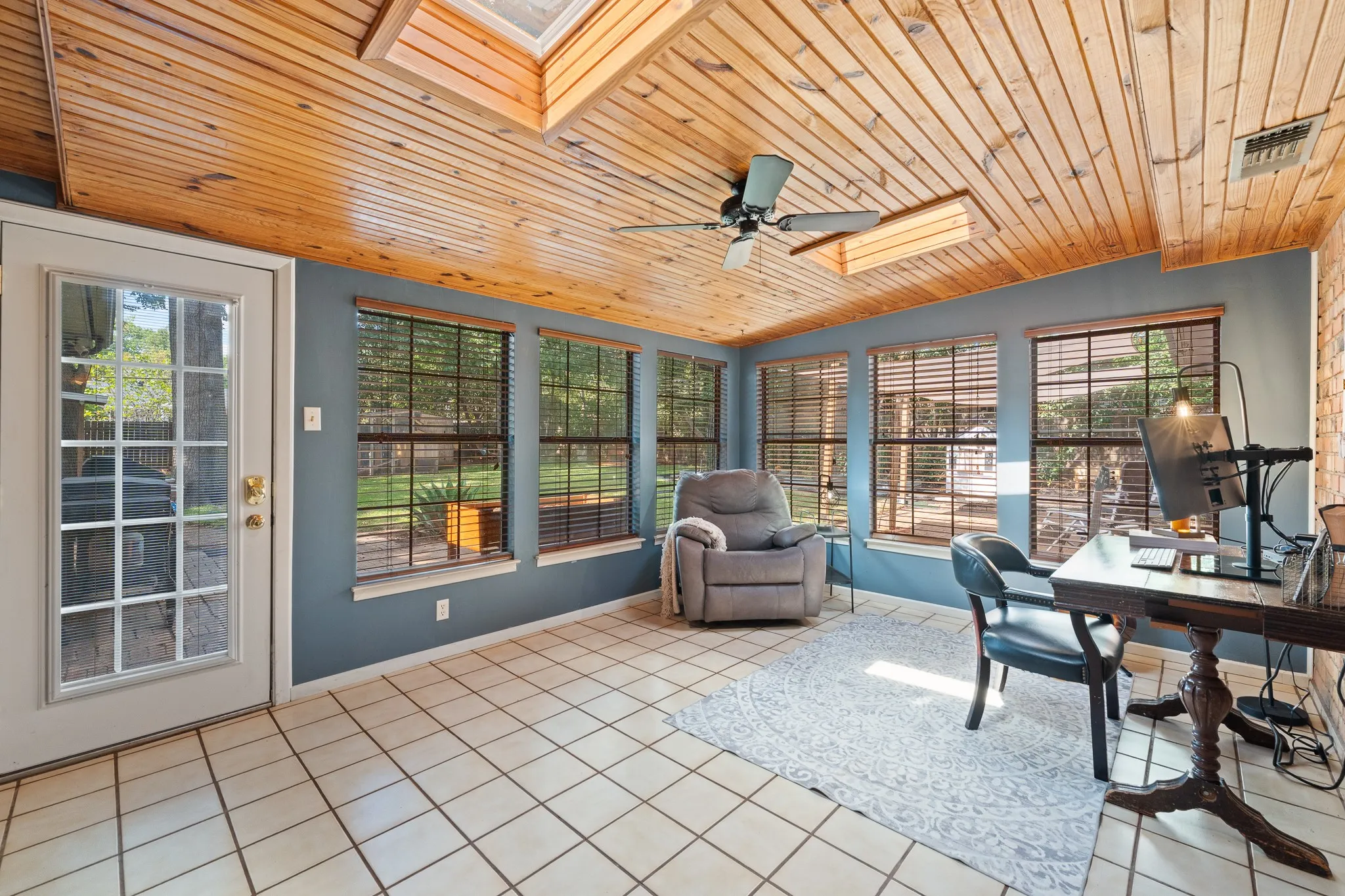 Room featuring a wood-panel ceiling, skylights, ceiling fan, tile flooring, and multiple windows with blinds