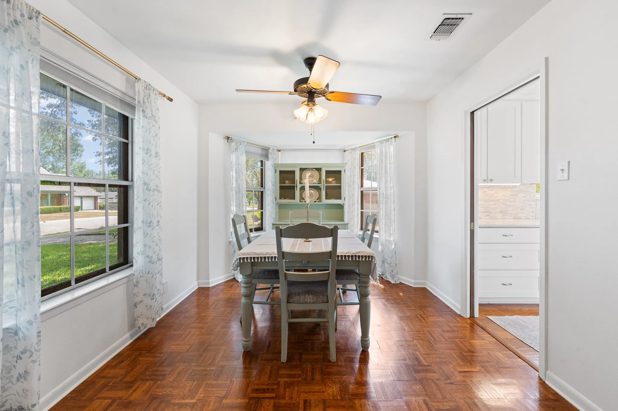 Parquet wood-finish flooring, bay window, ceiling fan, white cabinetry, and recessed lighting
