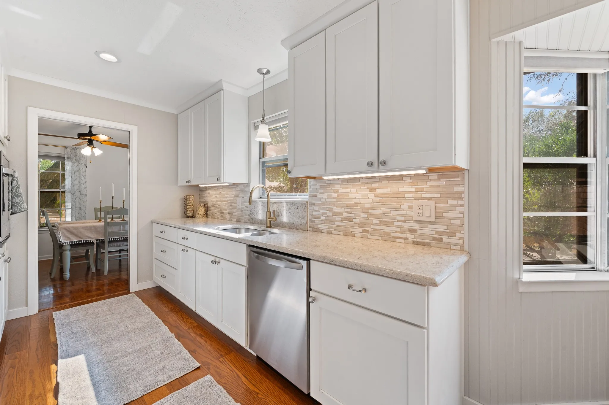 White shaker cabinetry, light-toned countertops, mosaic tile backsplash, stainless steel dishwasher, and wood-finish flooring
