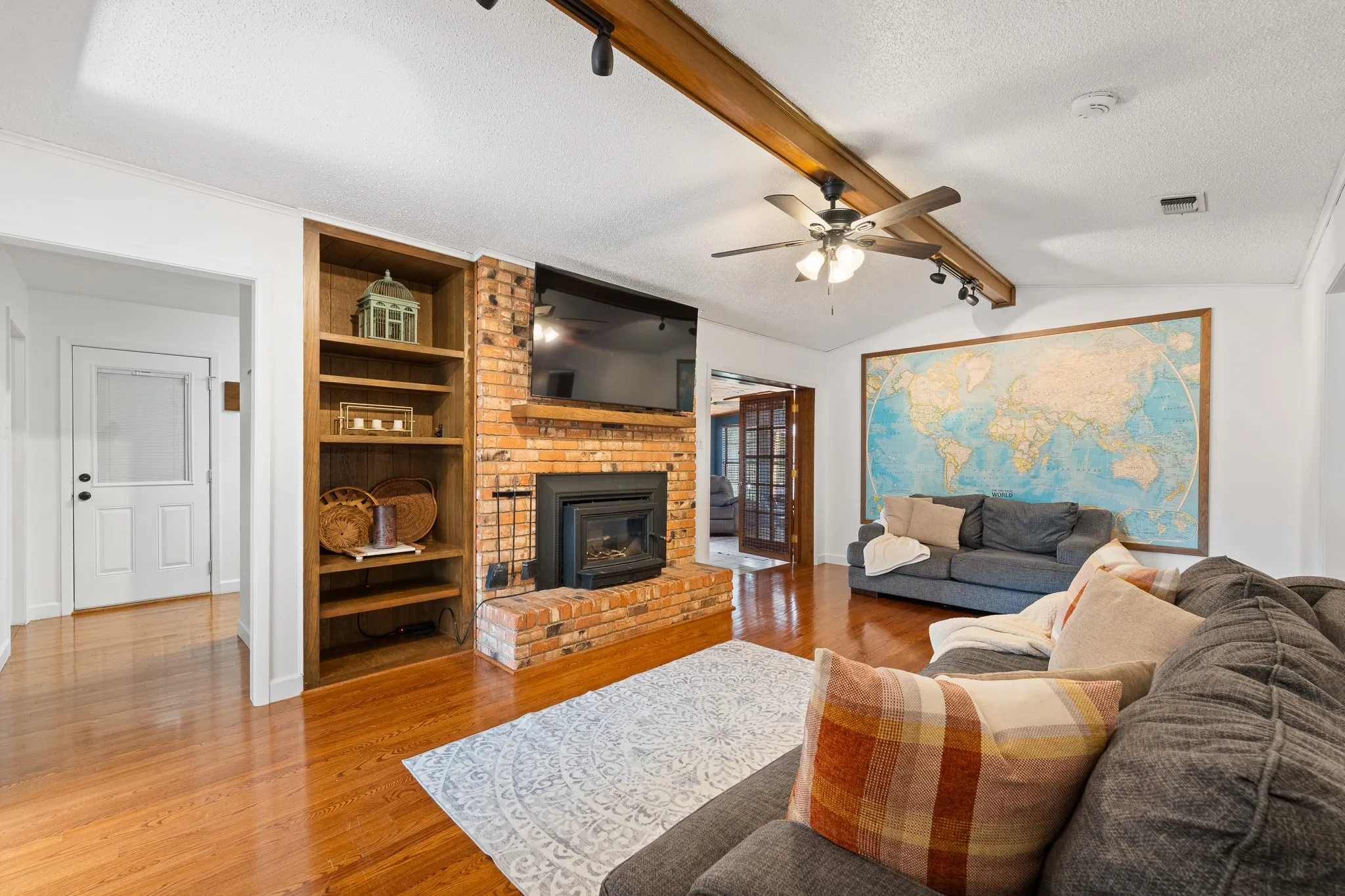 Wood-finish flooring throughout, with a brick fireplace and hearth, built-in shelving, and exposed ceiling beams