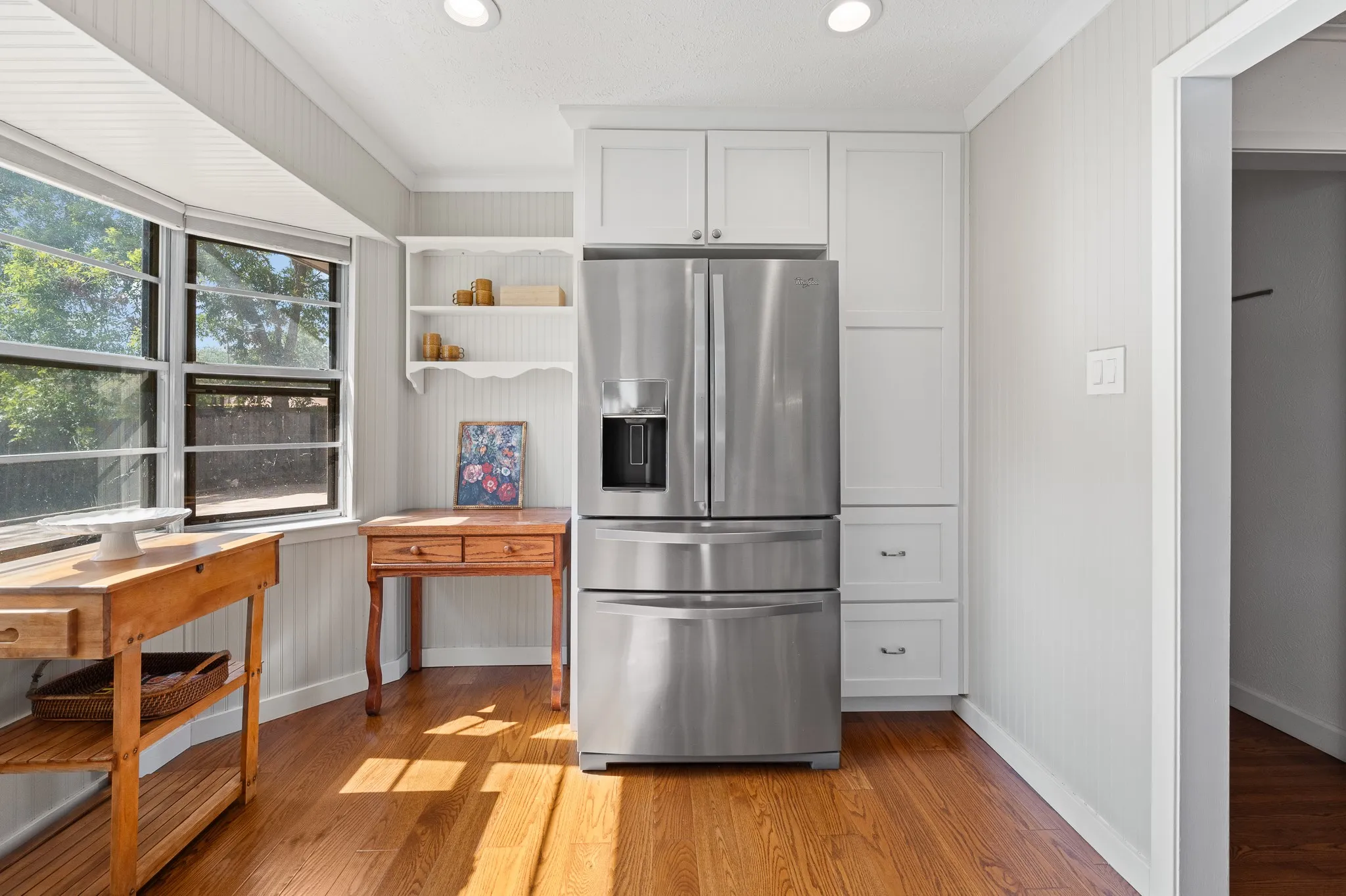Hardwood flooring with a bay window, stainless steel refrigerator, white shaker-style cabinetry, and recessed lighting