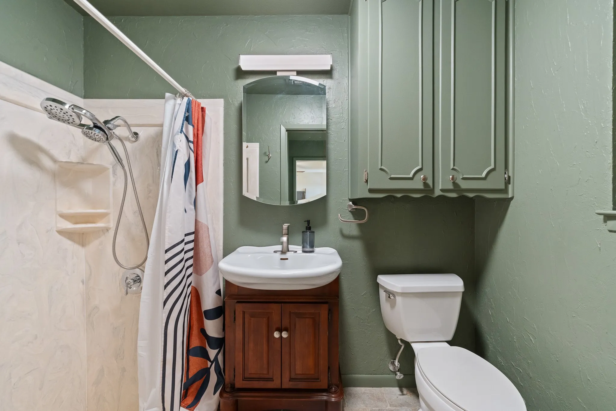 Wall-mounted cabinetry, pedestal sink with vanity, and a shower with a dual-function shower head