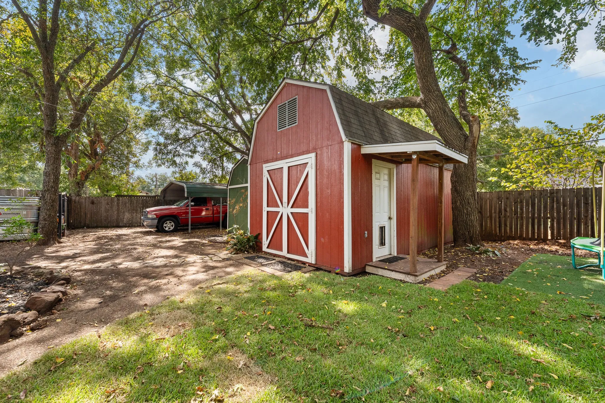 Detached red barn-style shed with white trim, covered front entry, and a side carport structure