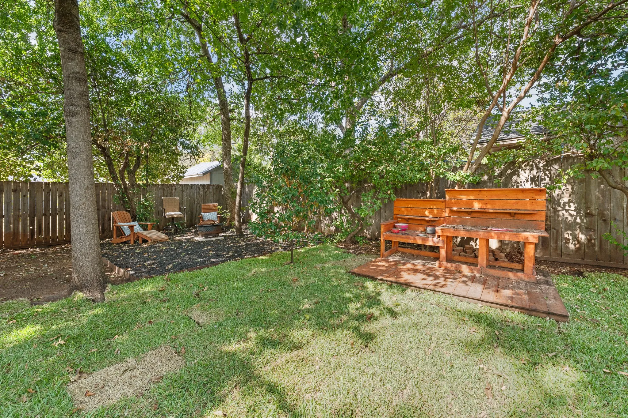 Expansive backyard featuring a manicured lawn, established trees, and a privacy fence