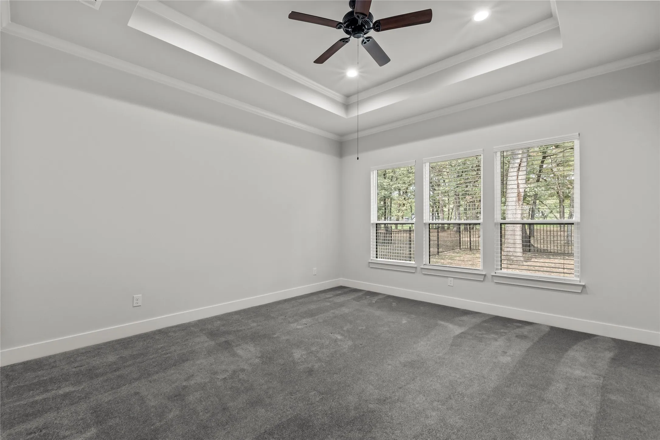 Tray ceiling with recessed lighting and a ceiling fan, three large windows, and neutral carpeting