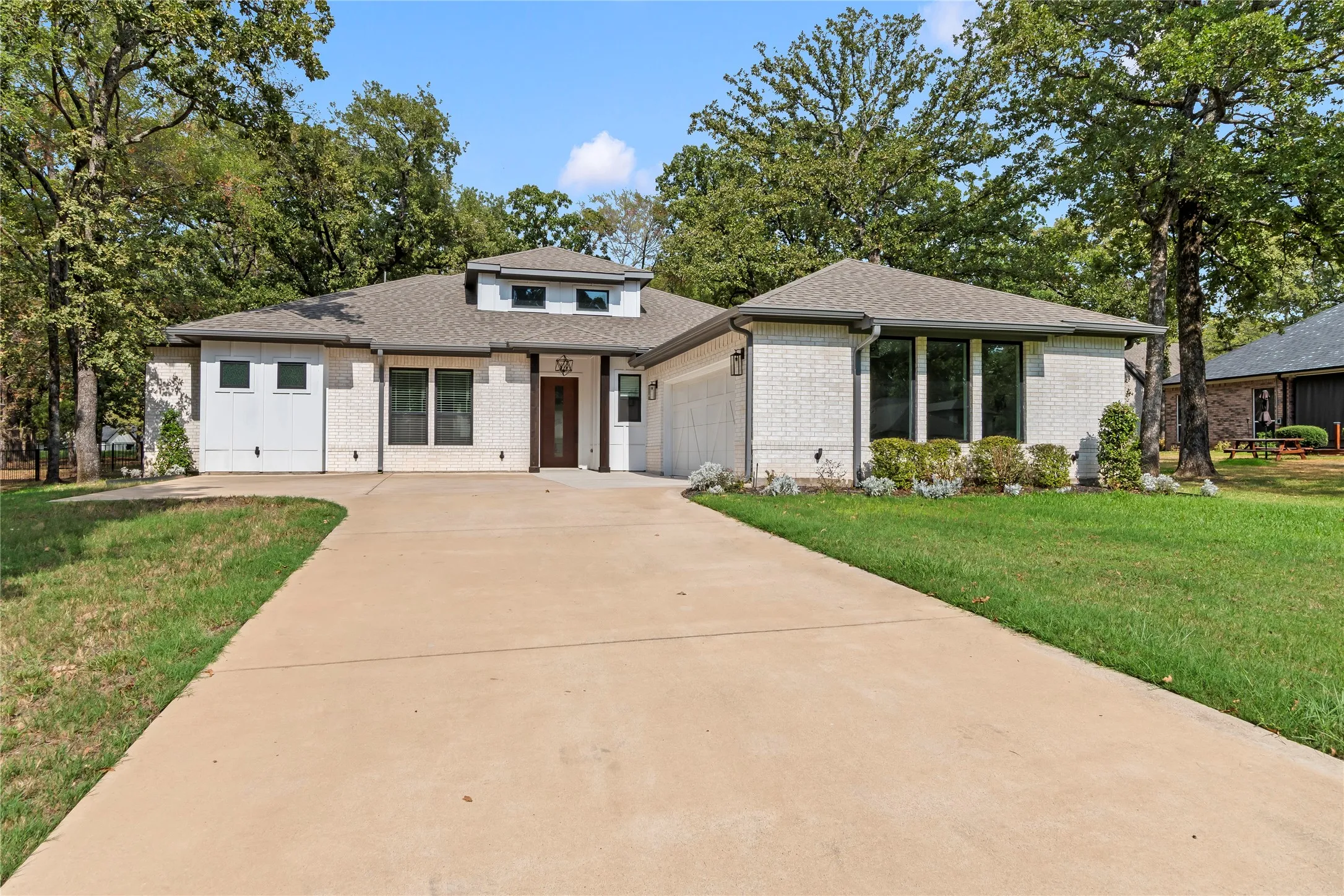 Contemporary exterior with light-colored brick, a dark wood-finish entry door, multiple large windows, and a concrete driveway