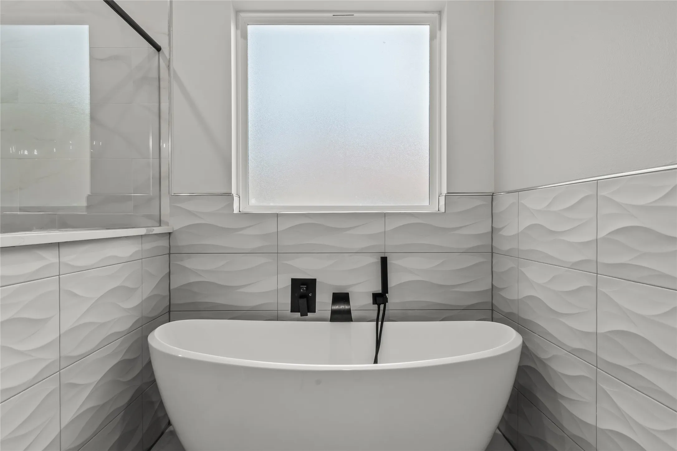 Modern spa-inspired soaking tub with matte black wall-mounted faucet and hand-shower fixture