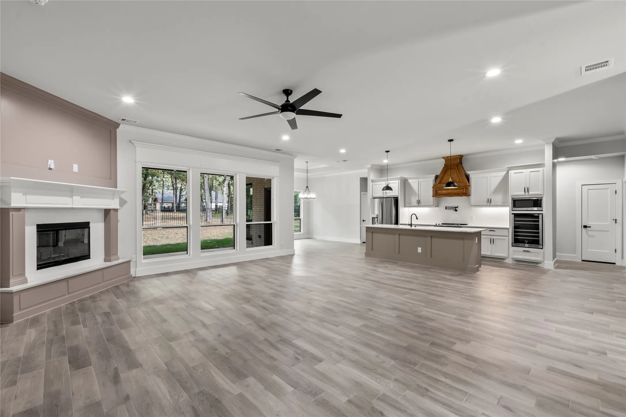 Open-concept living area featuring wood-finish flooring, a white mantel fireplace, and a kitchen with white cabinetry, a center island, and a wood-hood range