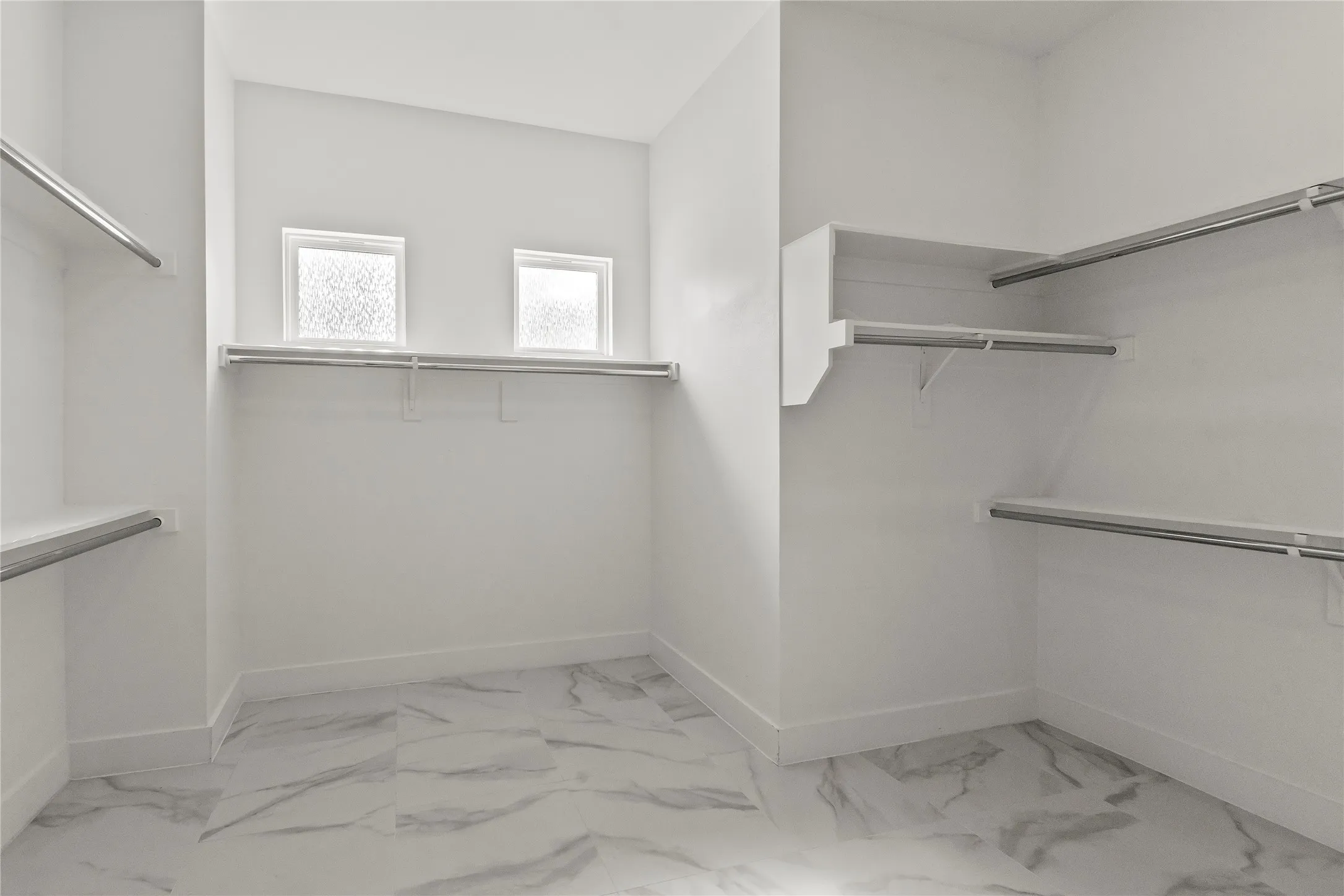 Walk-in closet featuring white walls, white-finish built-in shelving, two windows, and patterned tile flooring