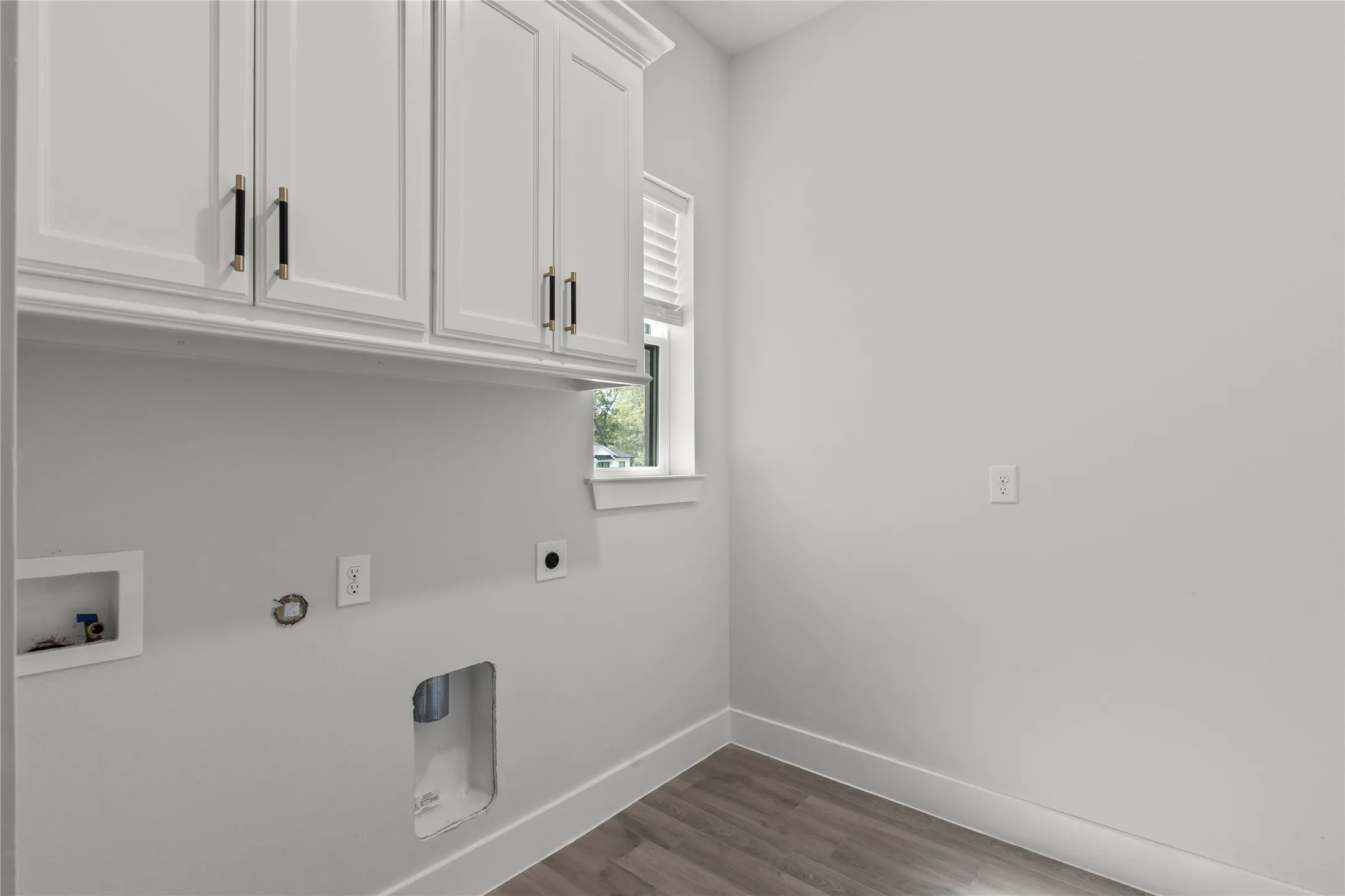 White shaker cabinetry with black hardware, wood-finish flooring, and a large window with blinds