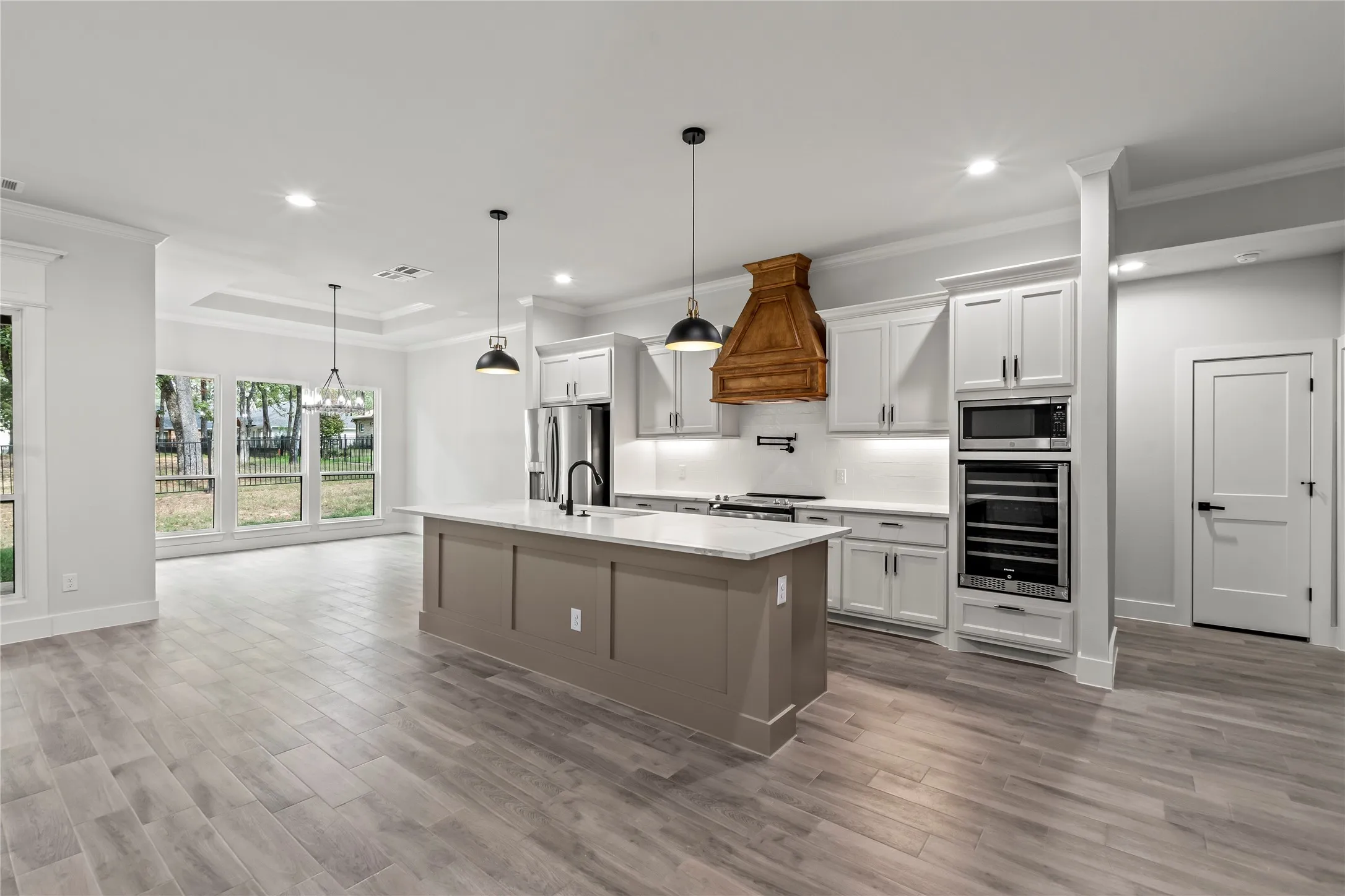 Spacious kitchen featuring an island with stone countertops, stainless steel appliances, a custom wood vent hood, and white cabinetry