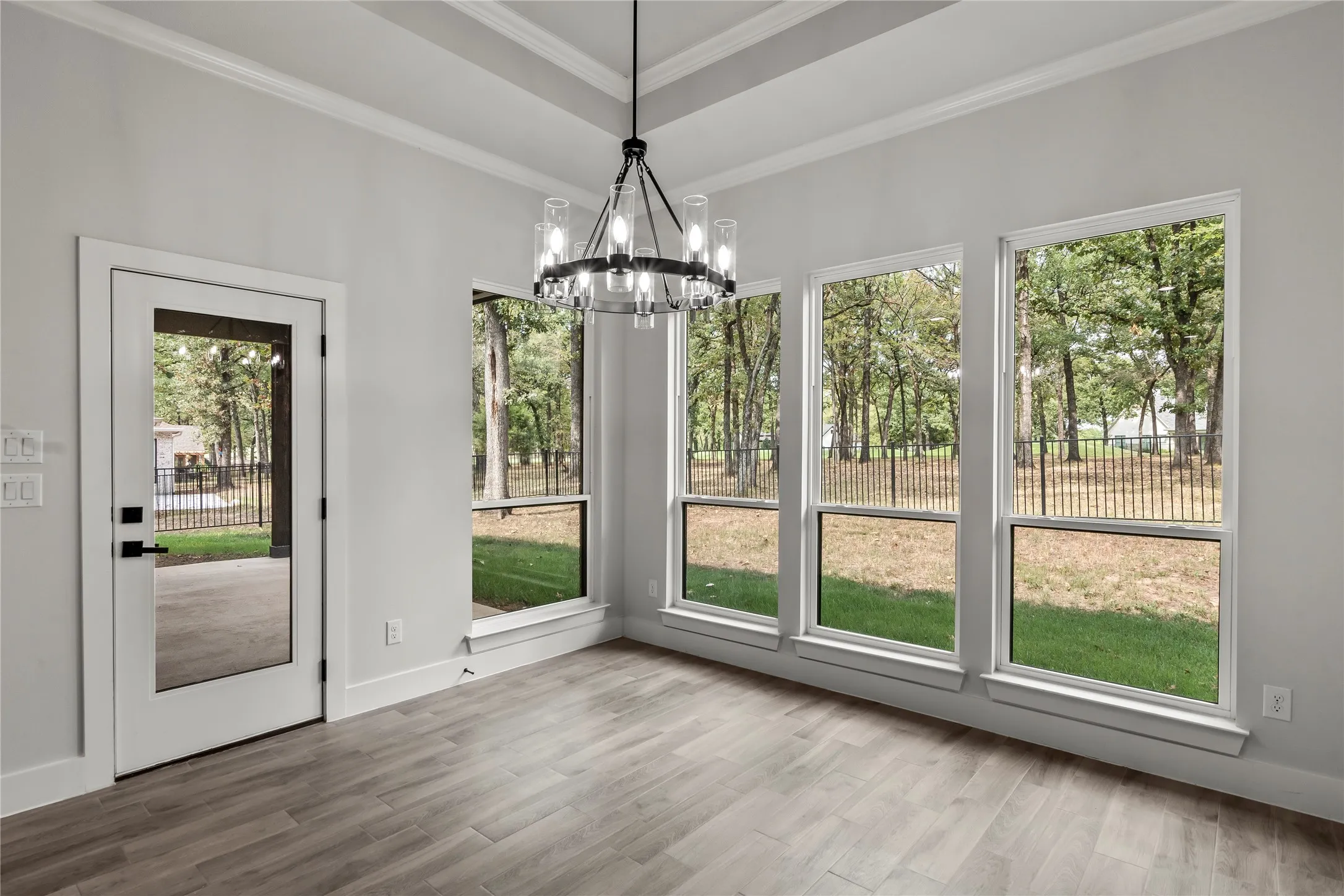 Tray ceiling with crown molding, wood-finish flooring, glass-paned exterior door, and multiple windows