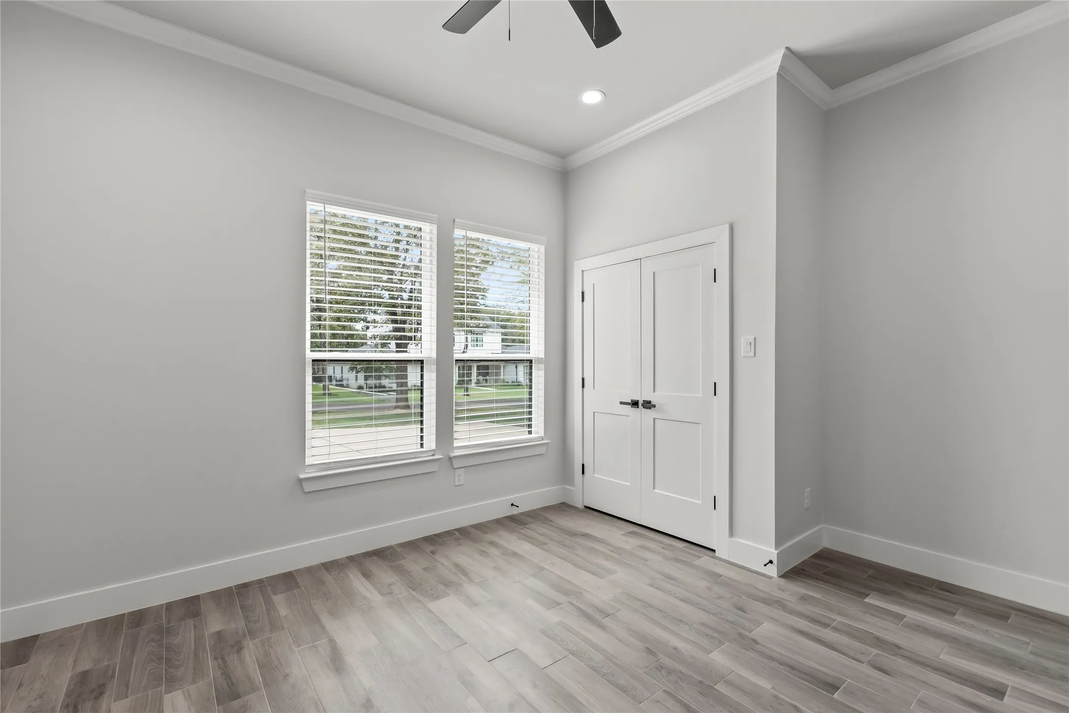 Neutral wall tones, wood-finish flooring, two large windows, white paneled doors, and a ceiling fan with integrated lighting