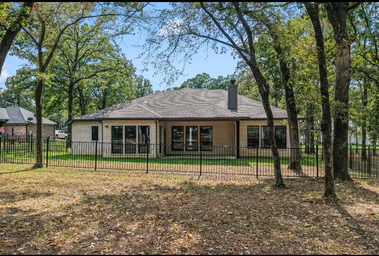 Brick exterior with a covered patio, multiple large windows, and a fenced yard