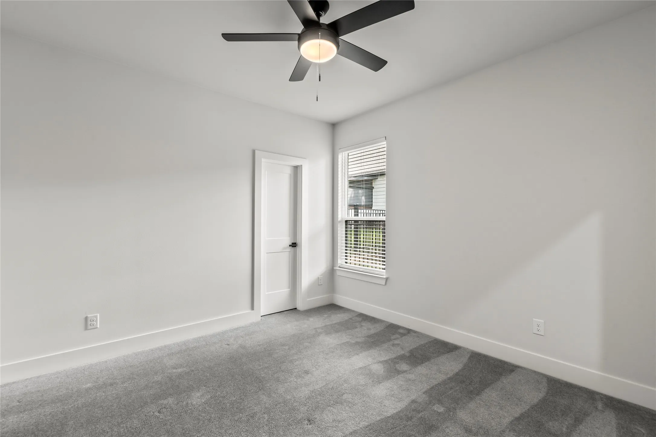 White walls with grey carpet, a white door, and a single window with blinds