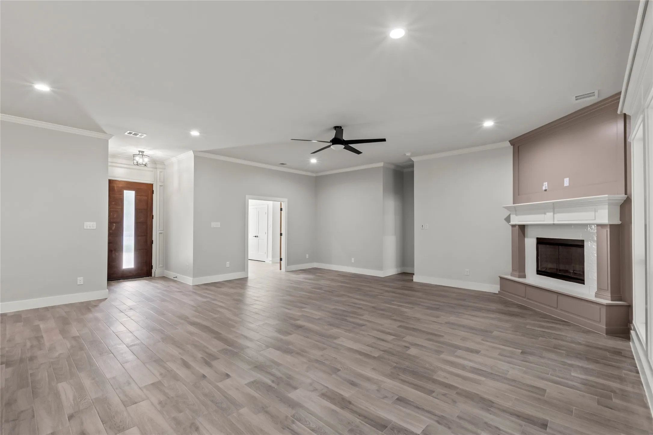 Spacious living area featuring wood-finish flooring, recessed lighting, and a corner fireplace with a white mantel