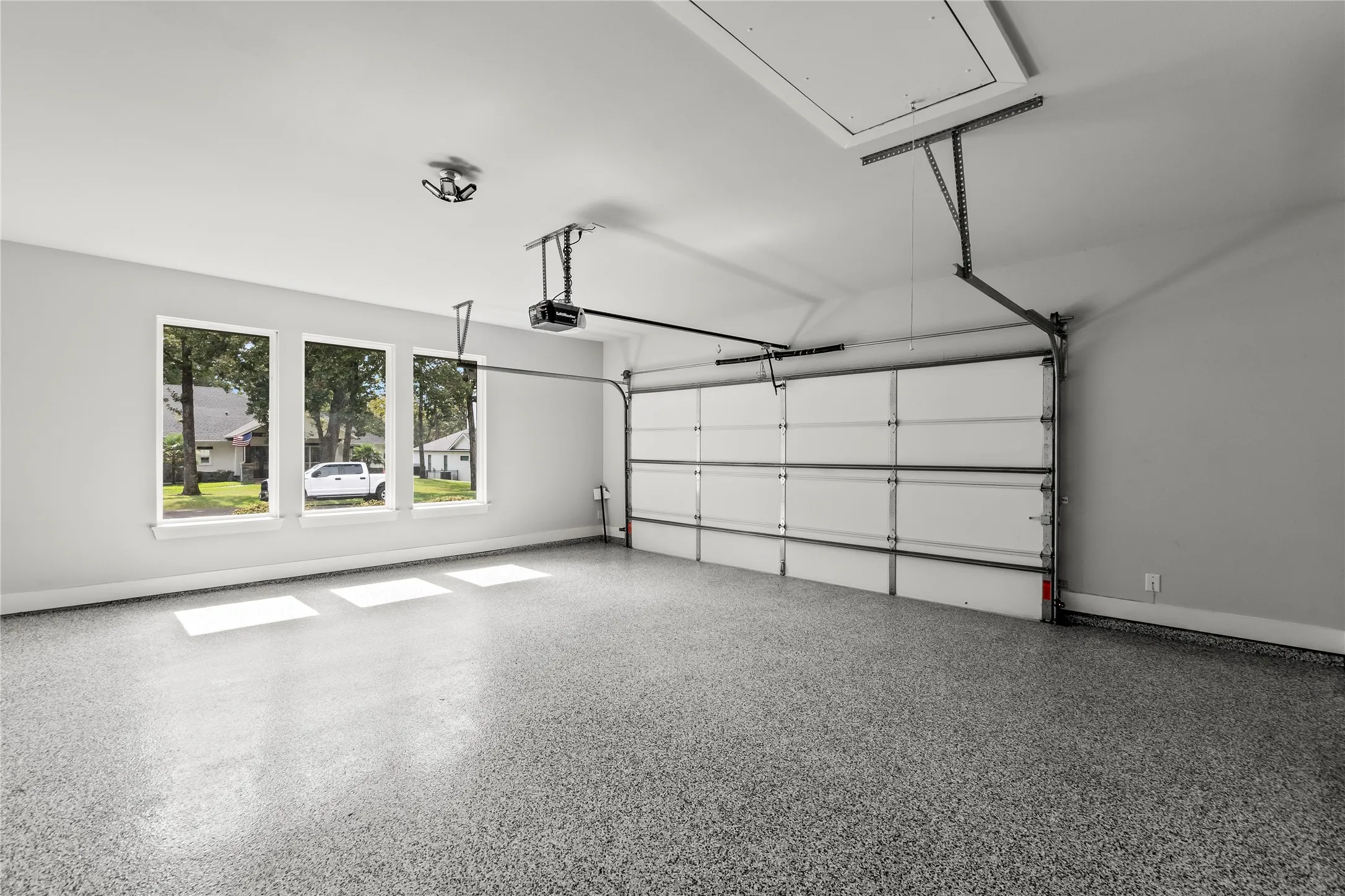 Garage with speckled epoxy flooring, three windows, an automatic garage door opener, and an attic access panel