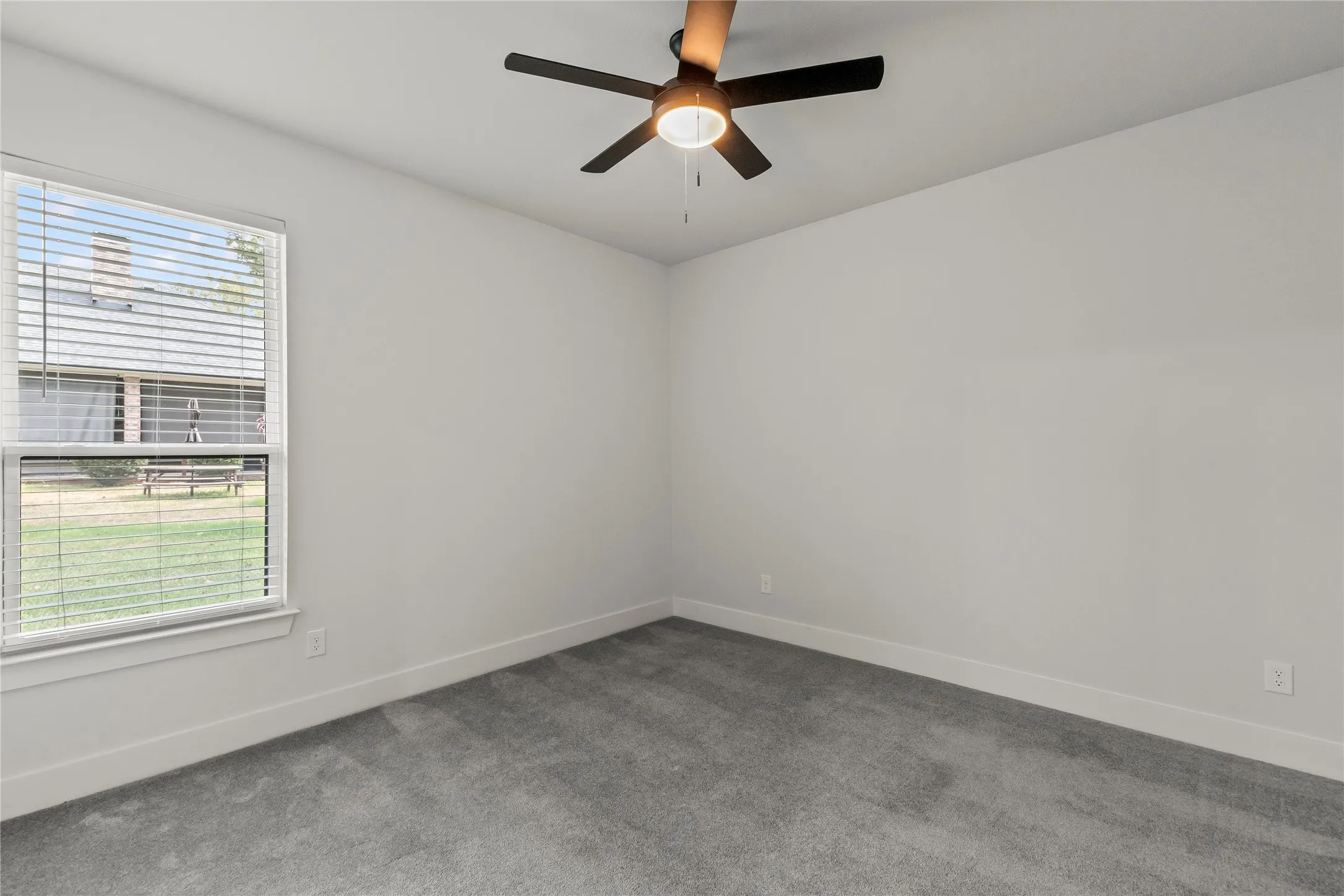 Bright bedroom featuring neutral wall finishes, plush carpeting, a ceiling fan with integrated lighting, and large double-hung window allowing natural light