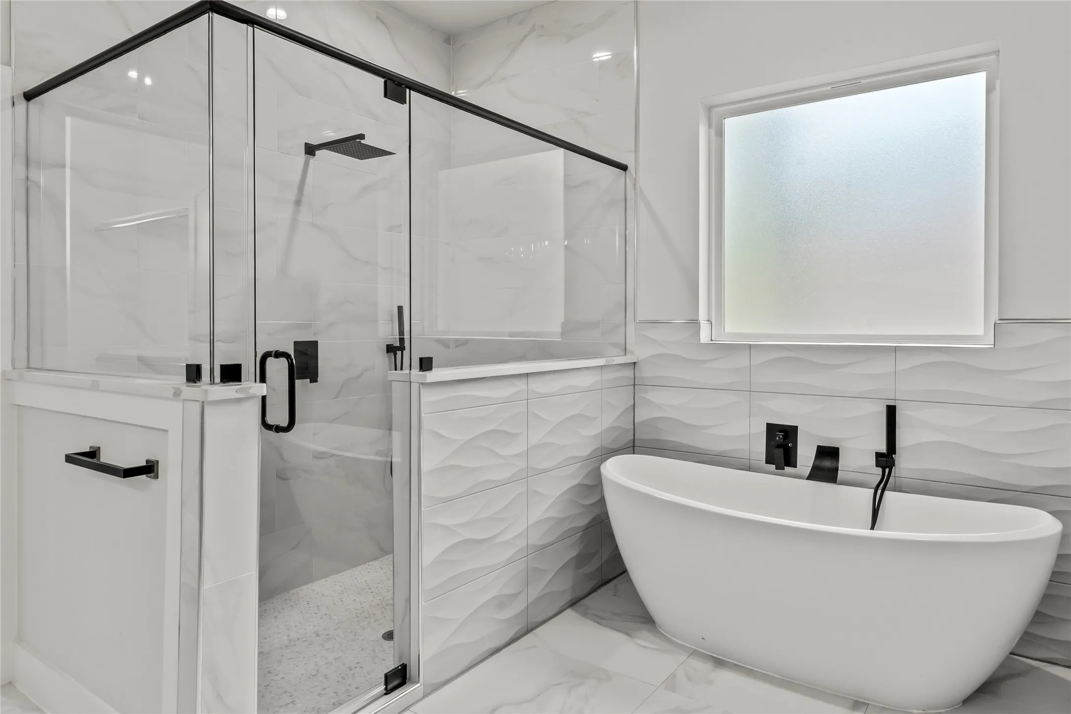 Freestanding soaking tub with matte black fixtures, separate glass-enclosed shower with matte black hardware, textured wall tiles, and large format floor tiles
